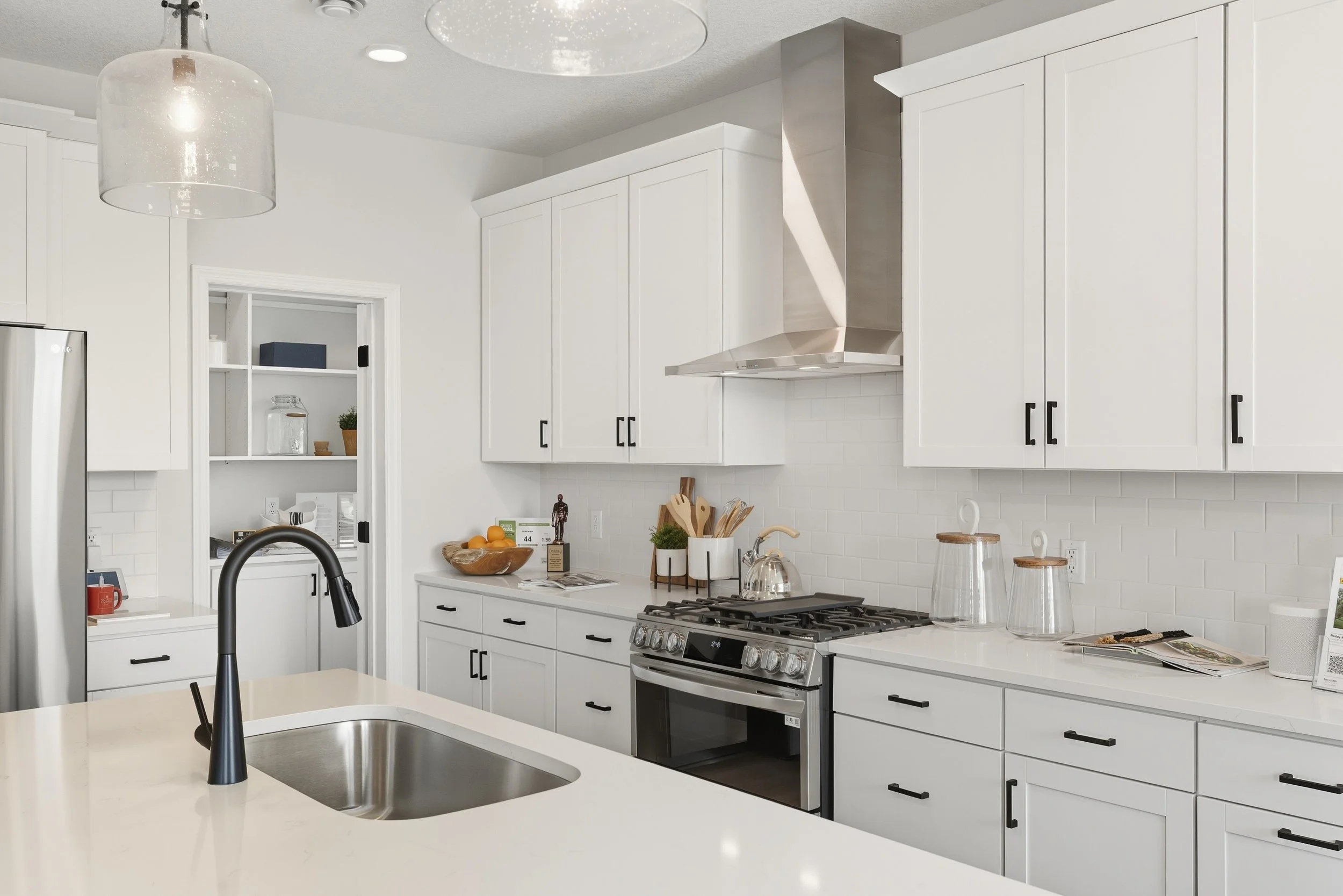 Modern kitchen with white cabinets, stainless steel appliances, black handles, a white countertop, and a black kitchen faucet.