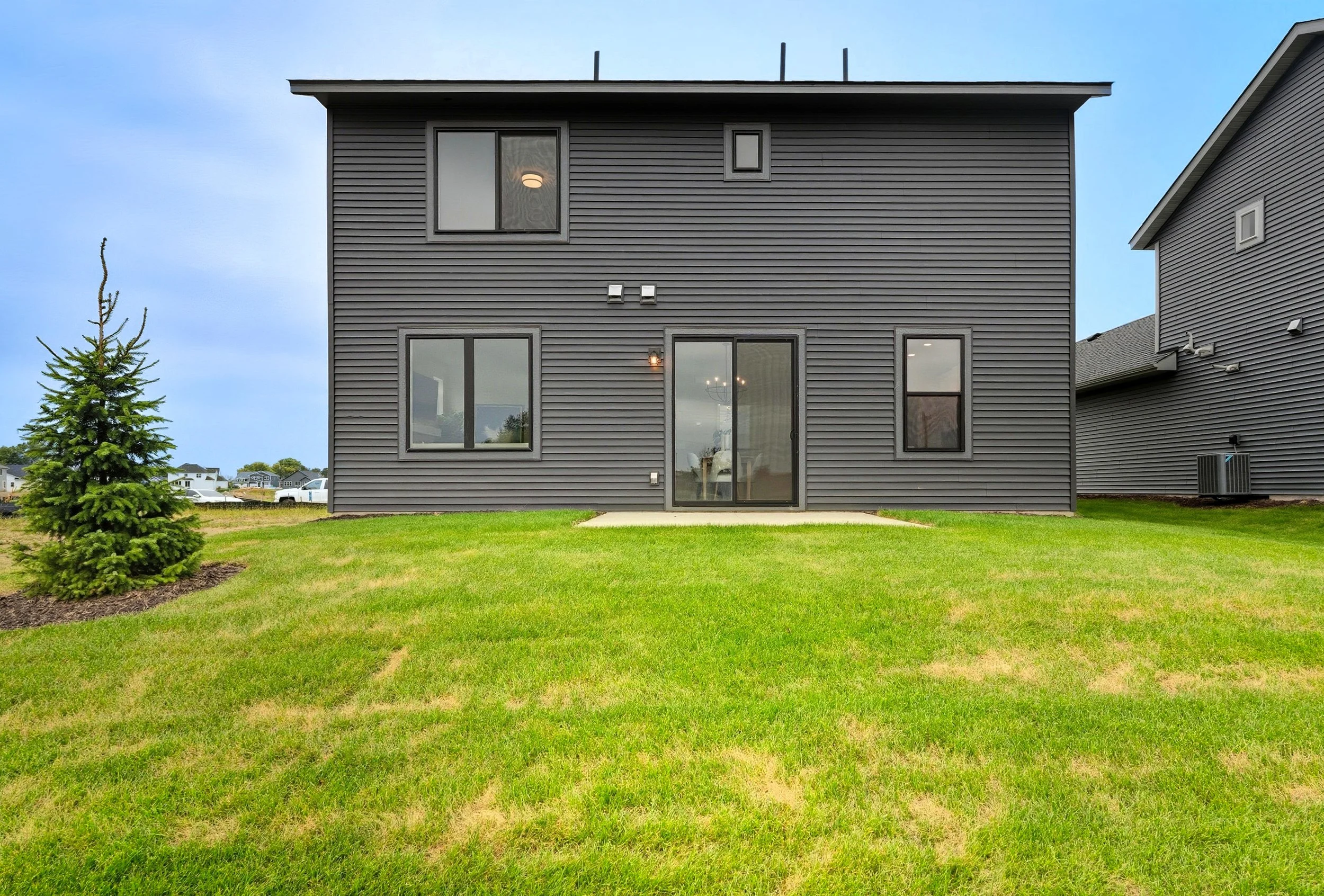 Rear view of a black two-story house with a sliding glass door and several windows, surrounded by a green lawn and a small tree on the left.