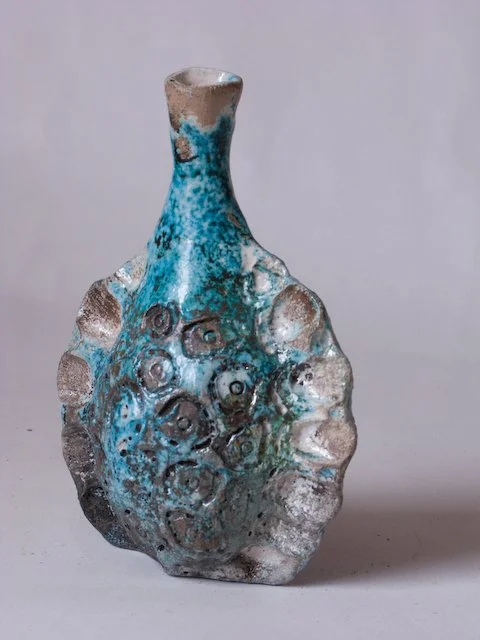 A ceramic vase with a narrow neck and a rounded body, decorated with blue, white, and brown glaze with textured, circular patterns.
