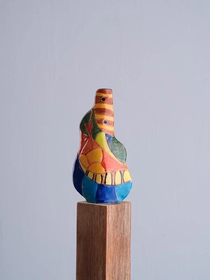 Colorful abstract ceramic sculpture on wooden pedestal against plain background