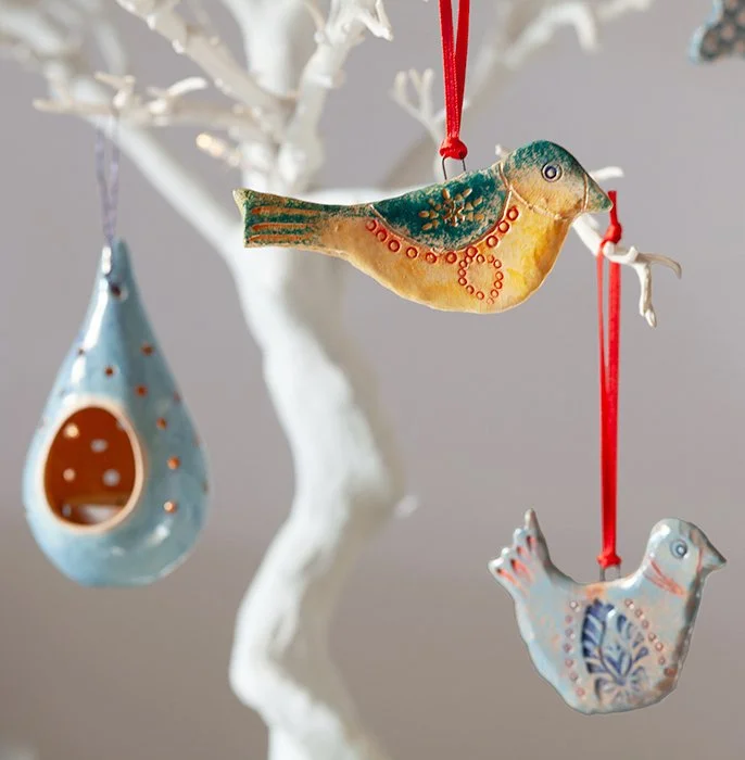 Decorative bird-themed ornaments hanging on a white tree branch, including a bird-shaped ornament with intricate patterns and a birdhouse with an oval entrance.