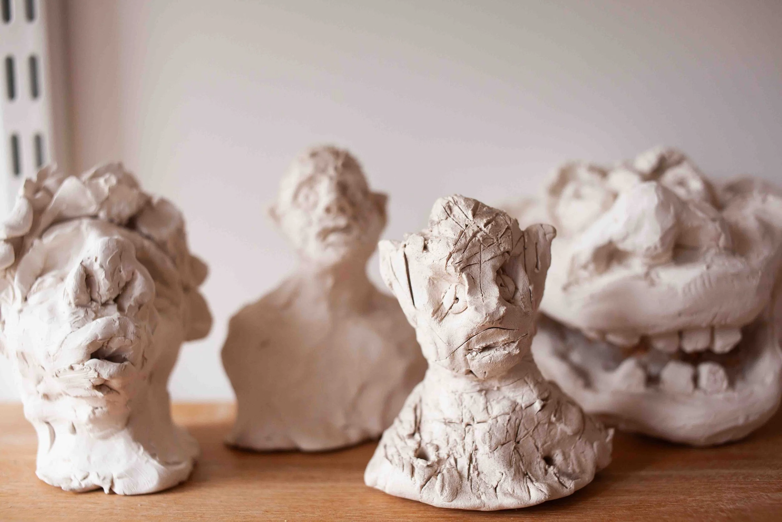 Close-up of several white clay sculptures of faces and busts on a wooden surface.