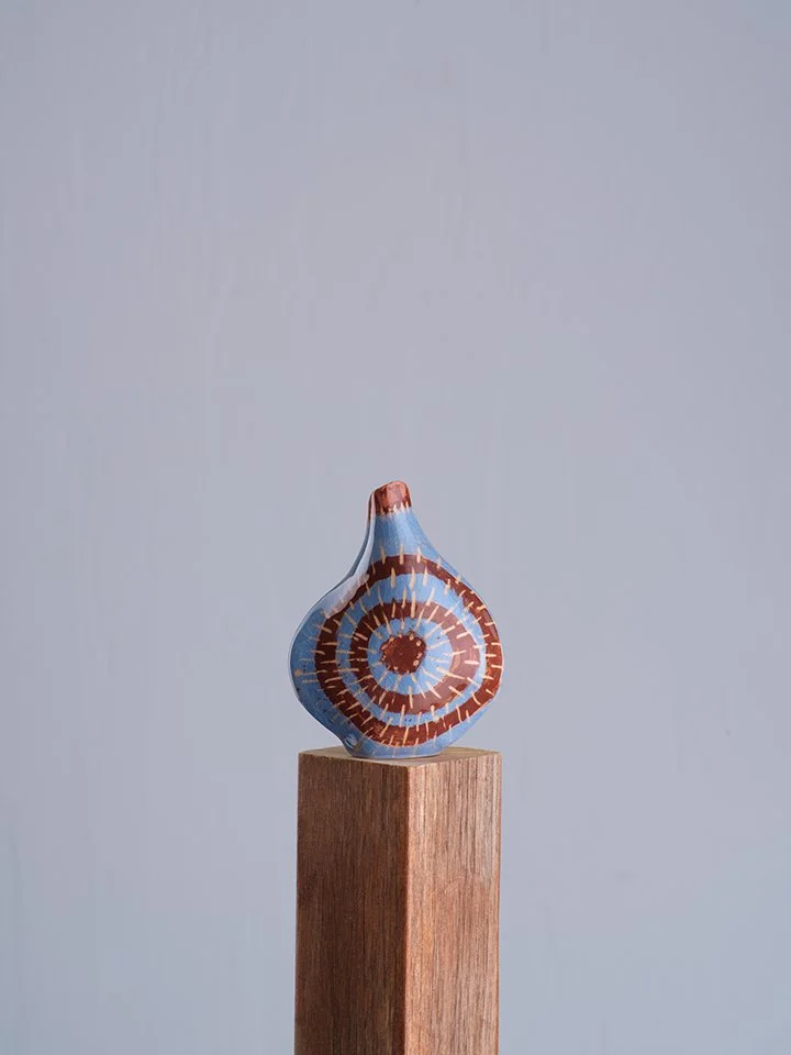 A decorative blue and brown swirled glass vase on a wooden pedestal against a plain gray background.