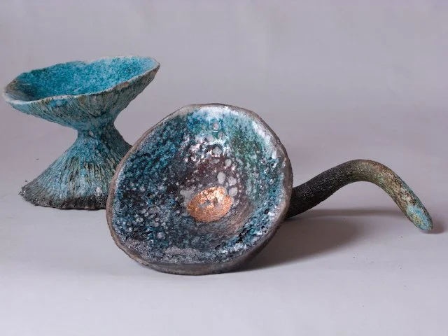 Two ceramic art sculptures resembling abstract flowers, one with a wide bowl-like top and the other with a curved stem, glazed in turquoise, blue, and metallic colors.