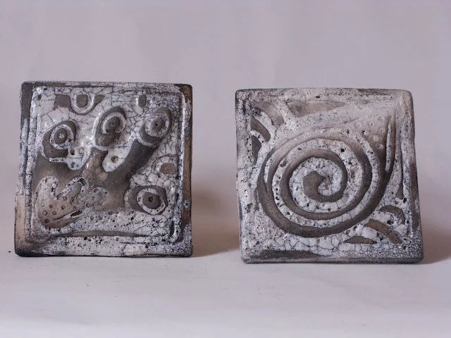 Two square metal stamps with carved spiral and abstract patterns.