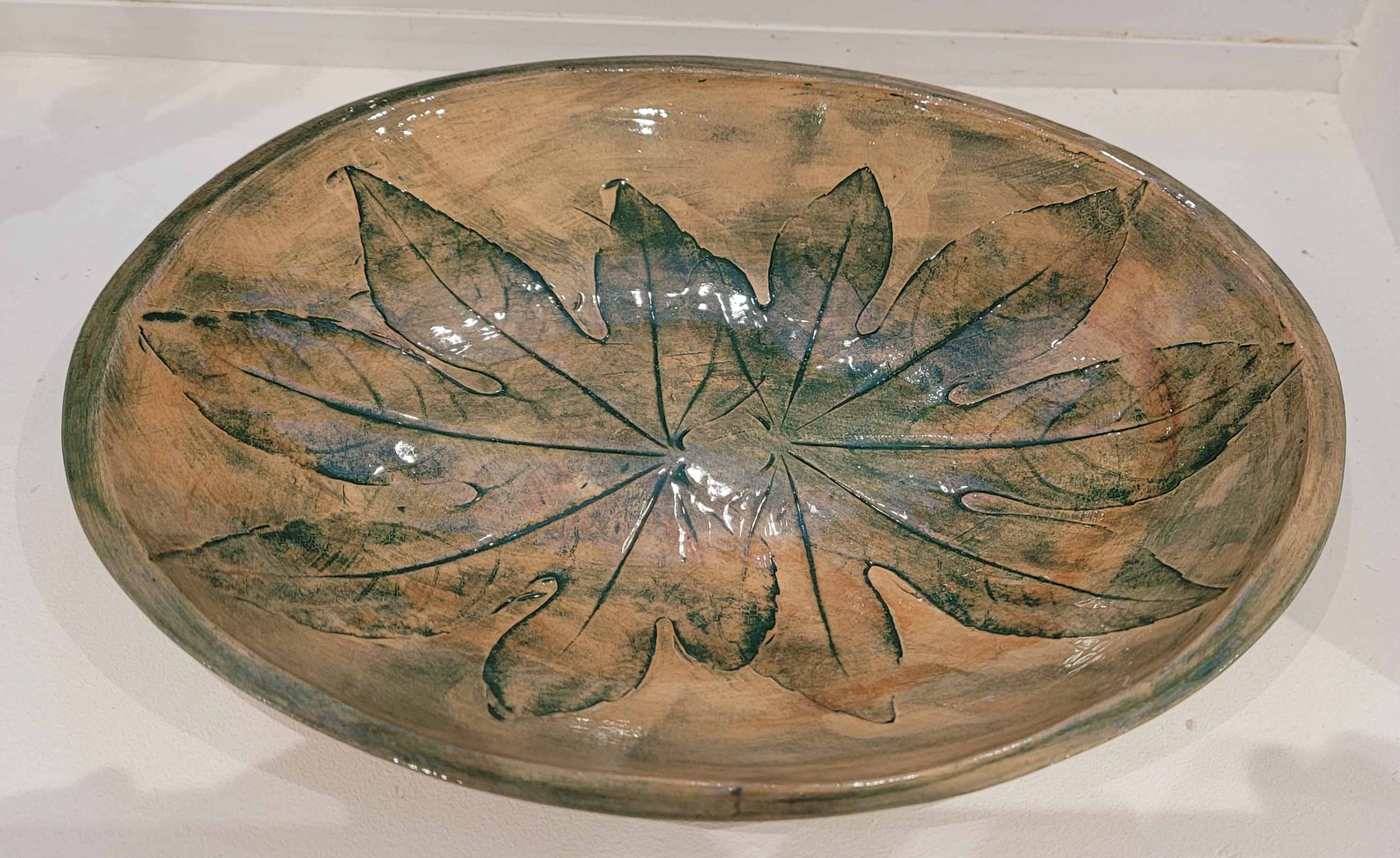Decorative oval ceramic bowl with leaf imprint design in earthy tones.