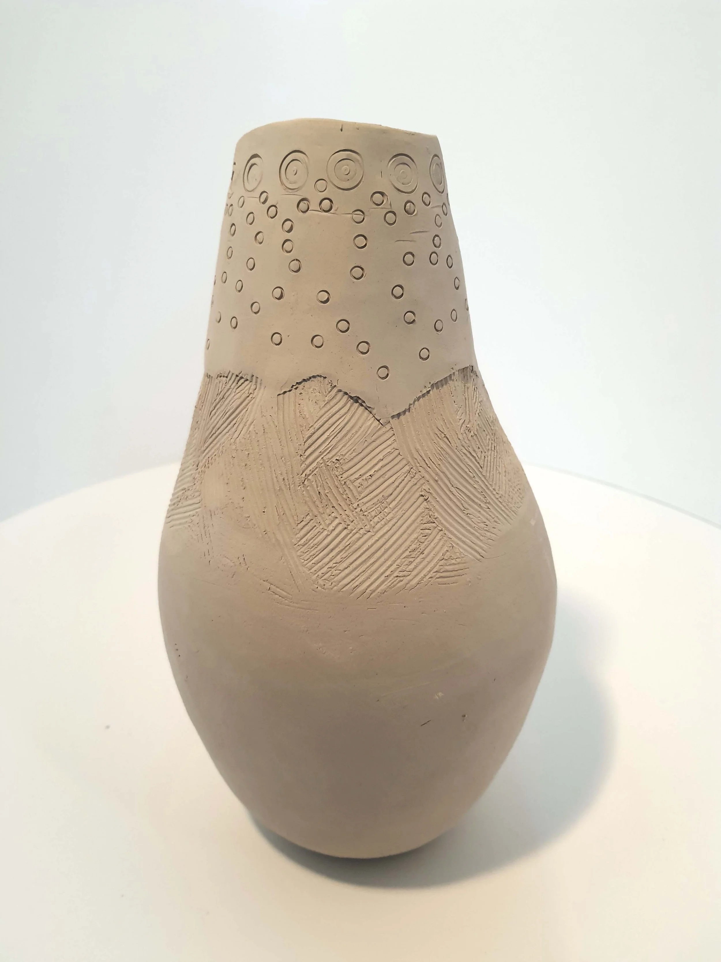 Ceramic vase with textured patterns and circular designs on the upper part, placed on a white surface with a plain white background.