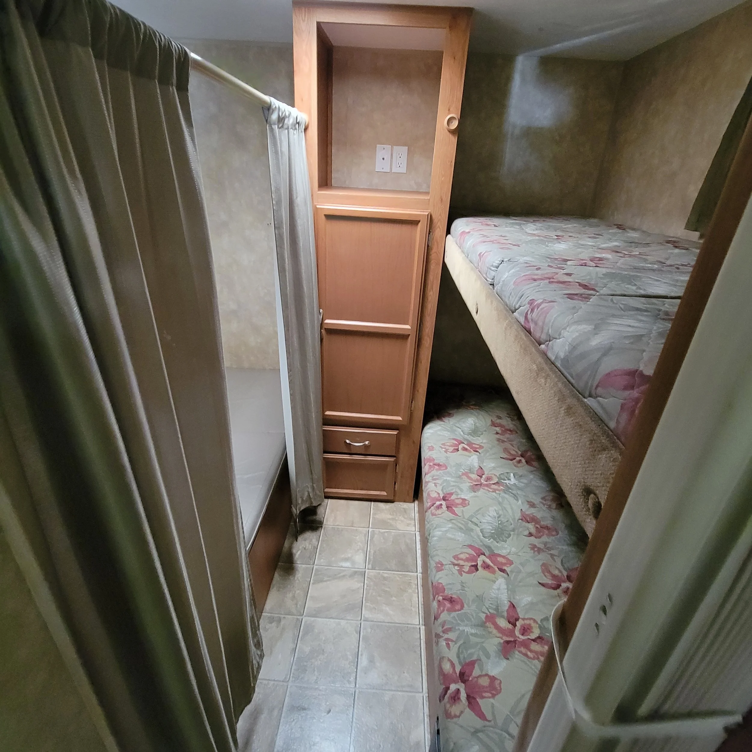 Small bedroom with bunk beds, floral patterned mattresses, a shower stall on the left, and built-in wooden cabinets on the back wall.