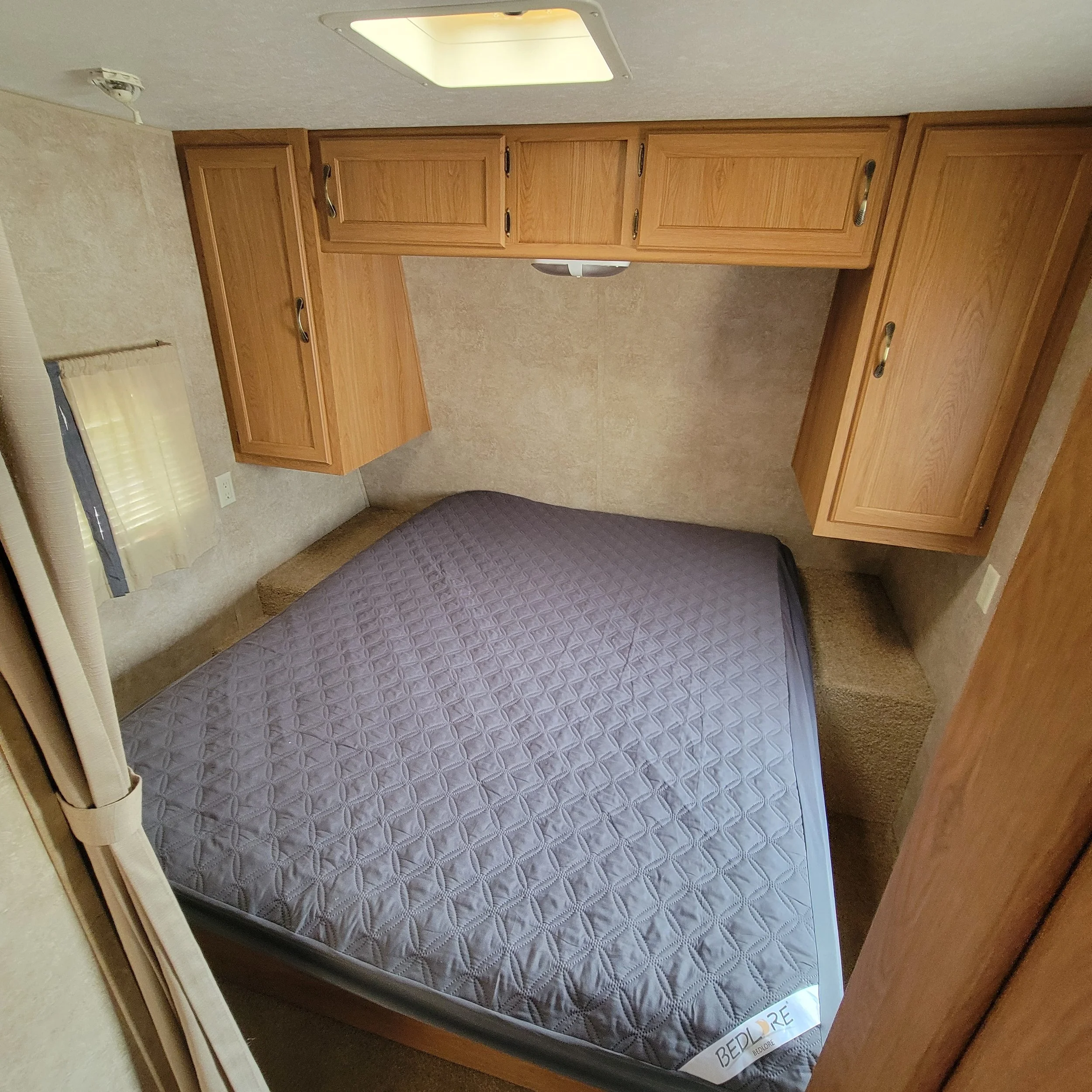 Compact bedroom with a bed and built-in wooden cabinets along the wall above and beside the bed.