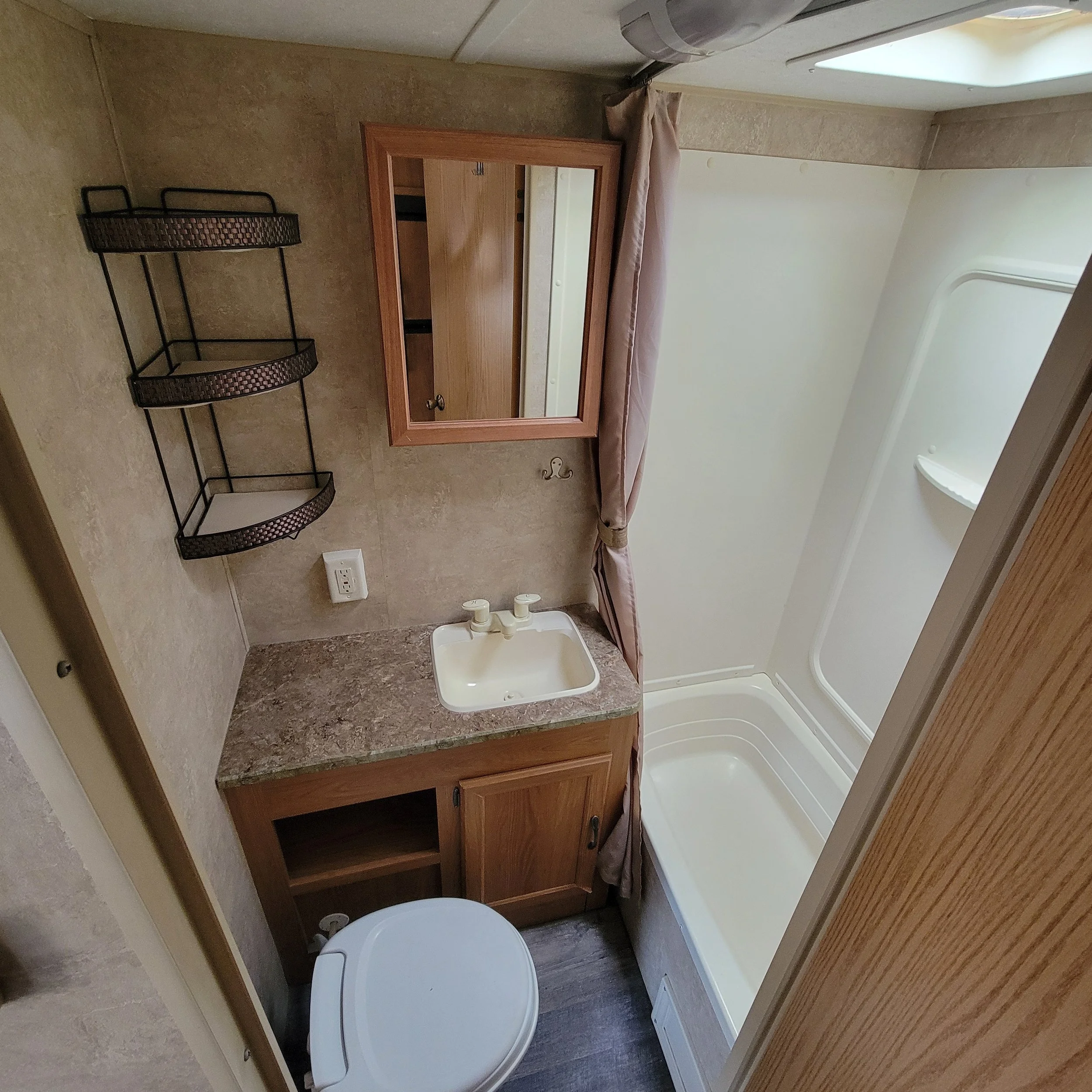 Small bathroom with a shower, sink with a cabinet underneath, a mirror, a towel hook, a corner shelf, and a toilet.