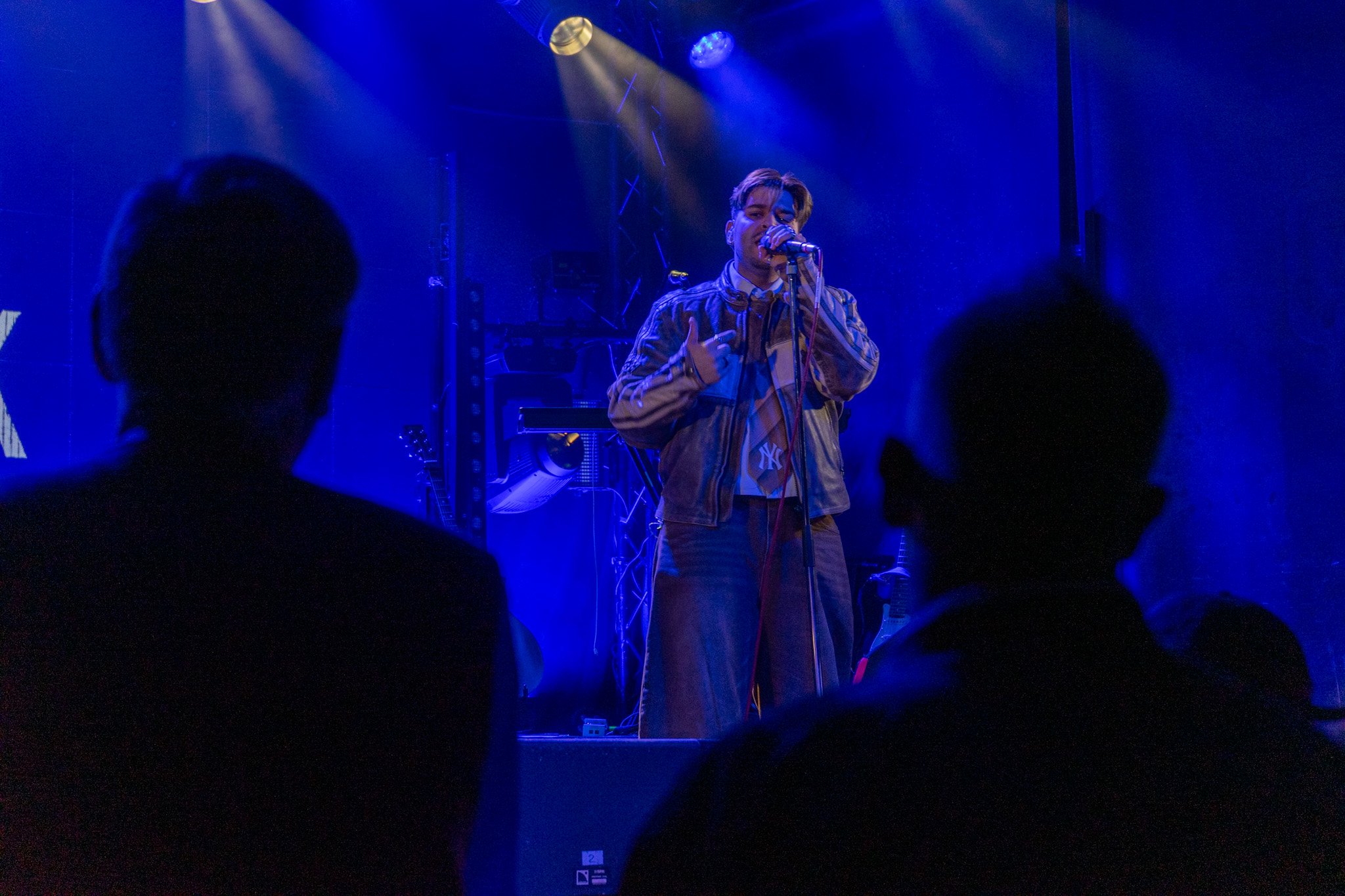 A singer performing on stage with blue lighting, holding a microphone and wearing a striped jacket, with audience members in the foreground.