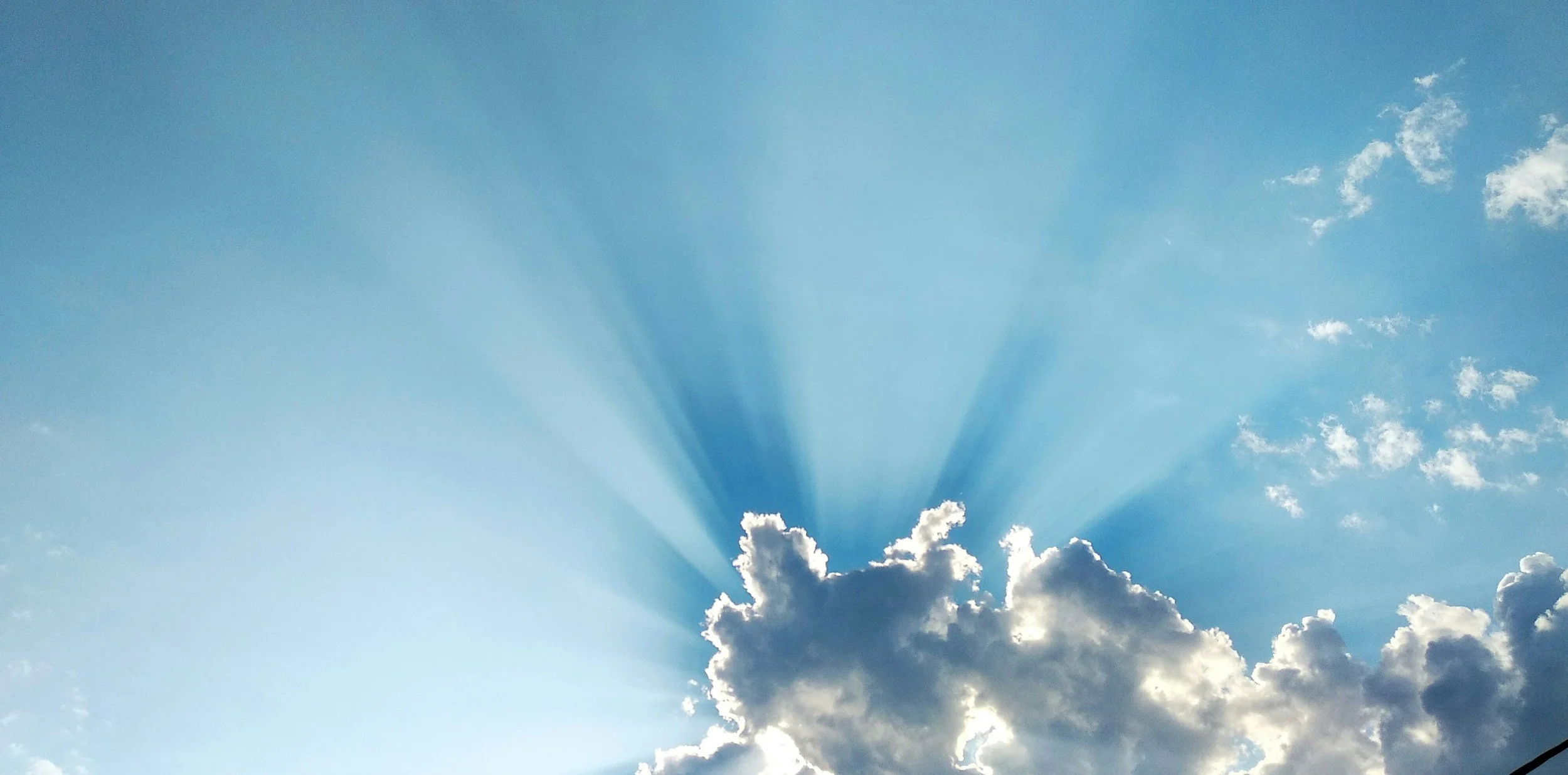 Blue sky with sunlight rays streaming through clouds.