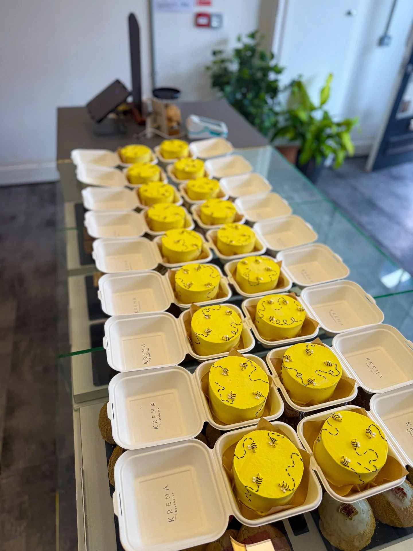 A table with multiple white takeout containers filled with yellow cakes decorated with small edible bees.