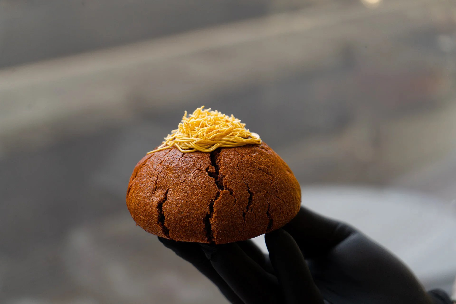 A person's hand holding a large cookie topped with shredded cheese and melted cheese.