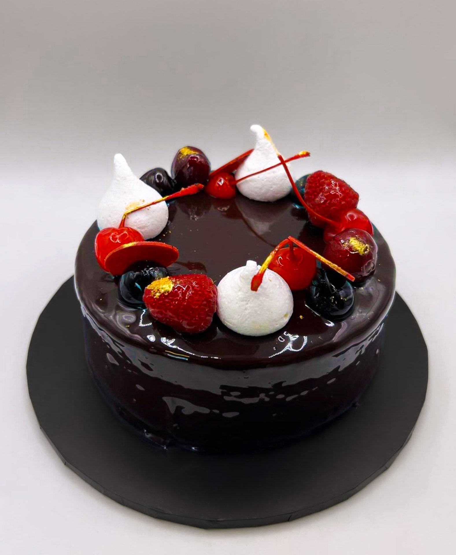 Chocolate-glazed cake decorated with strawberries, cherries, blueberries, meringue, and gold leaf.