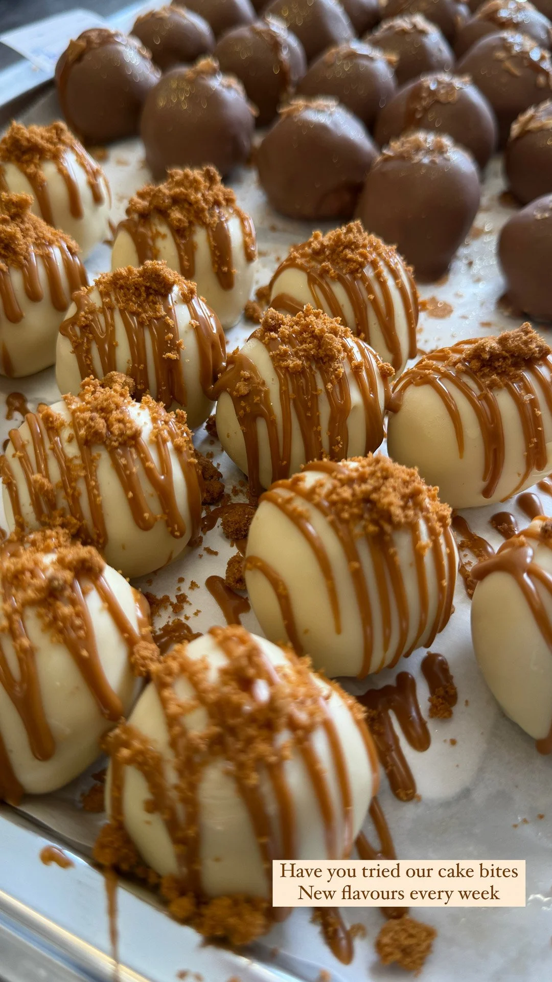 Close-up of white chocolate cake bites drizzled with caramel and topped with crushed cookies, with chocolate cake bites in the background.