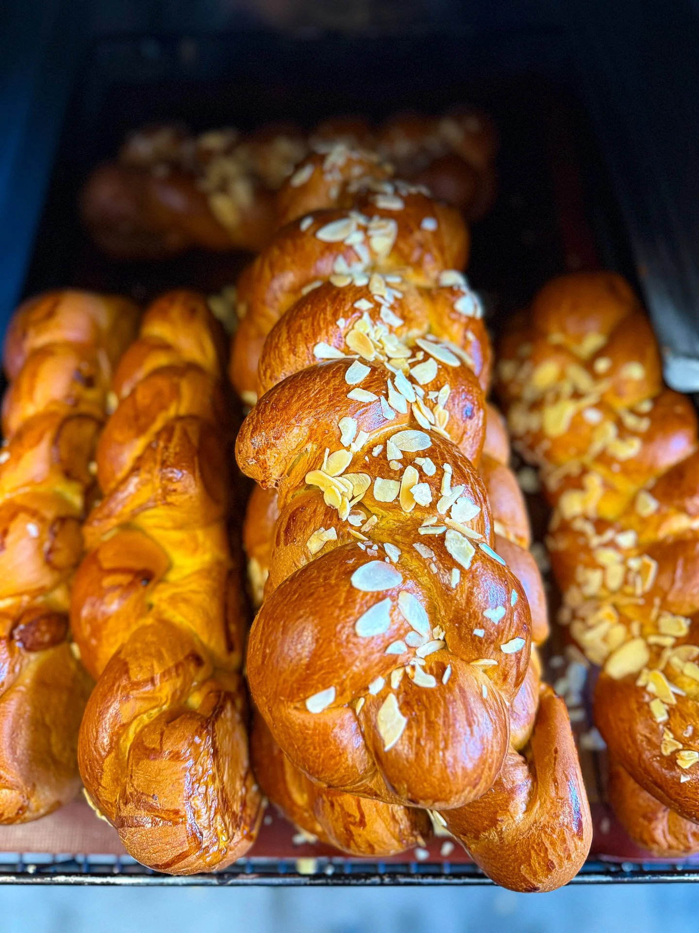 Fresh golden brown almond croissants topped with sliced almonds, displayed on a baking tray.