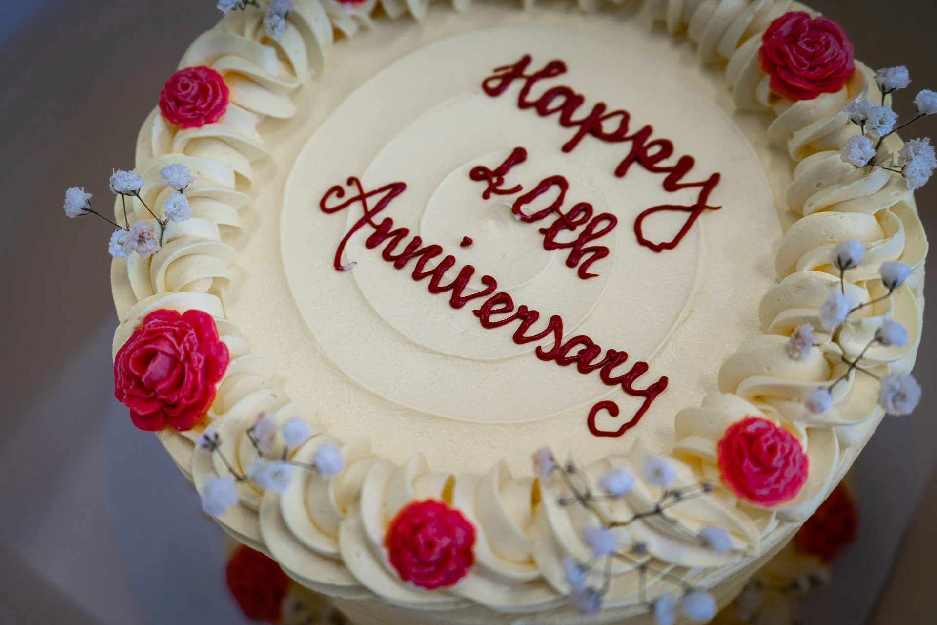 Round white cake with red and pink flowers, white icing swirls, and red writing that says "Happy Lord Thanksgiving".