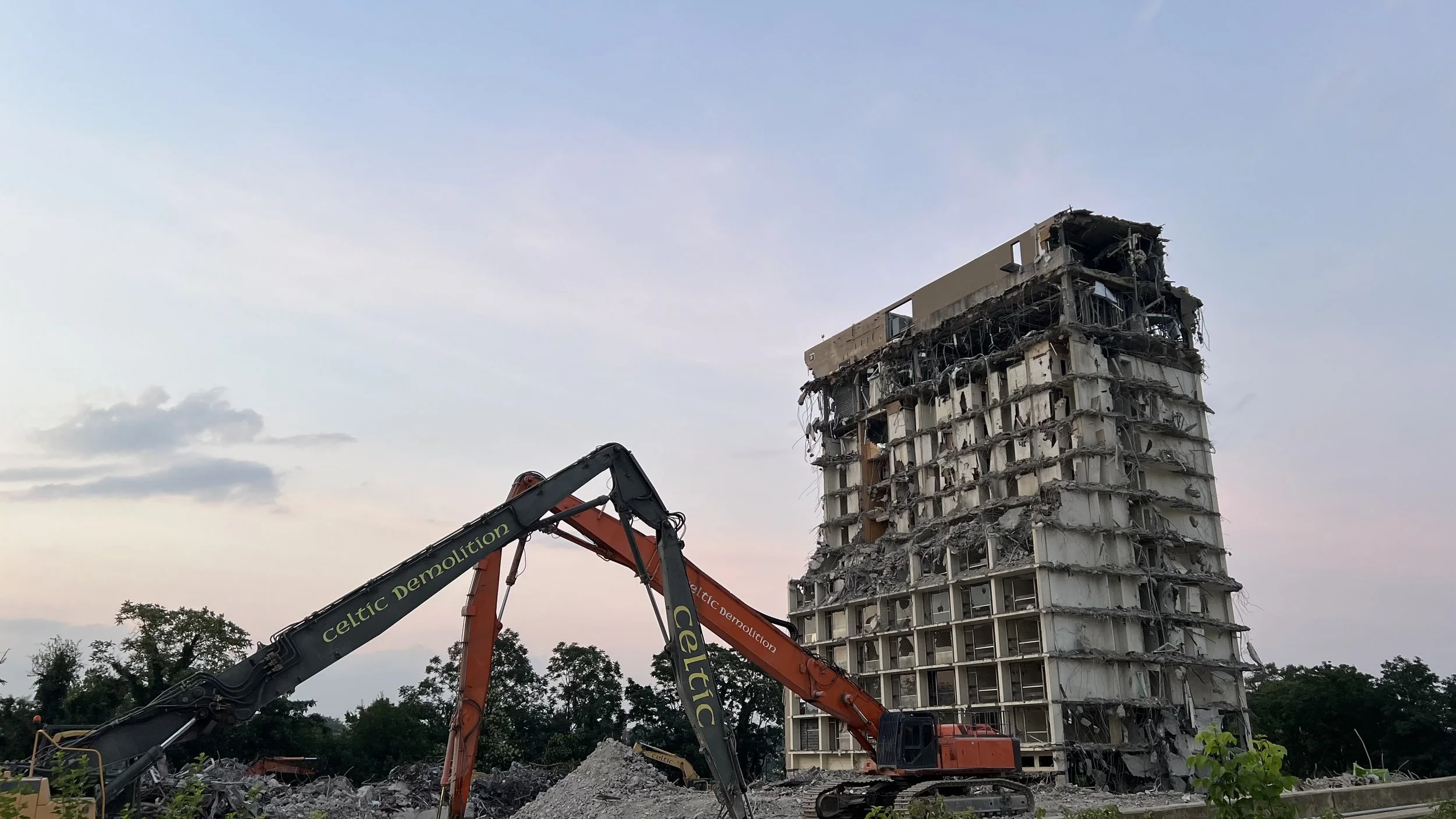 A partially demolished high-rise building with construction equipment in foreground.