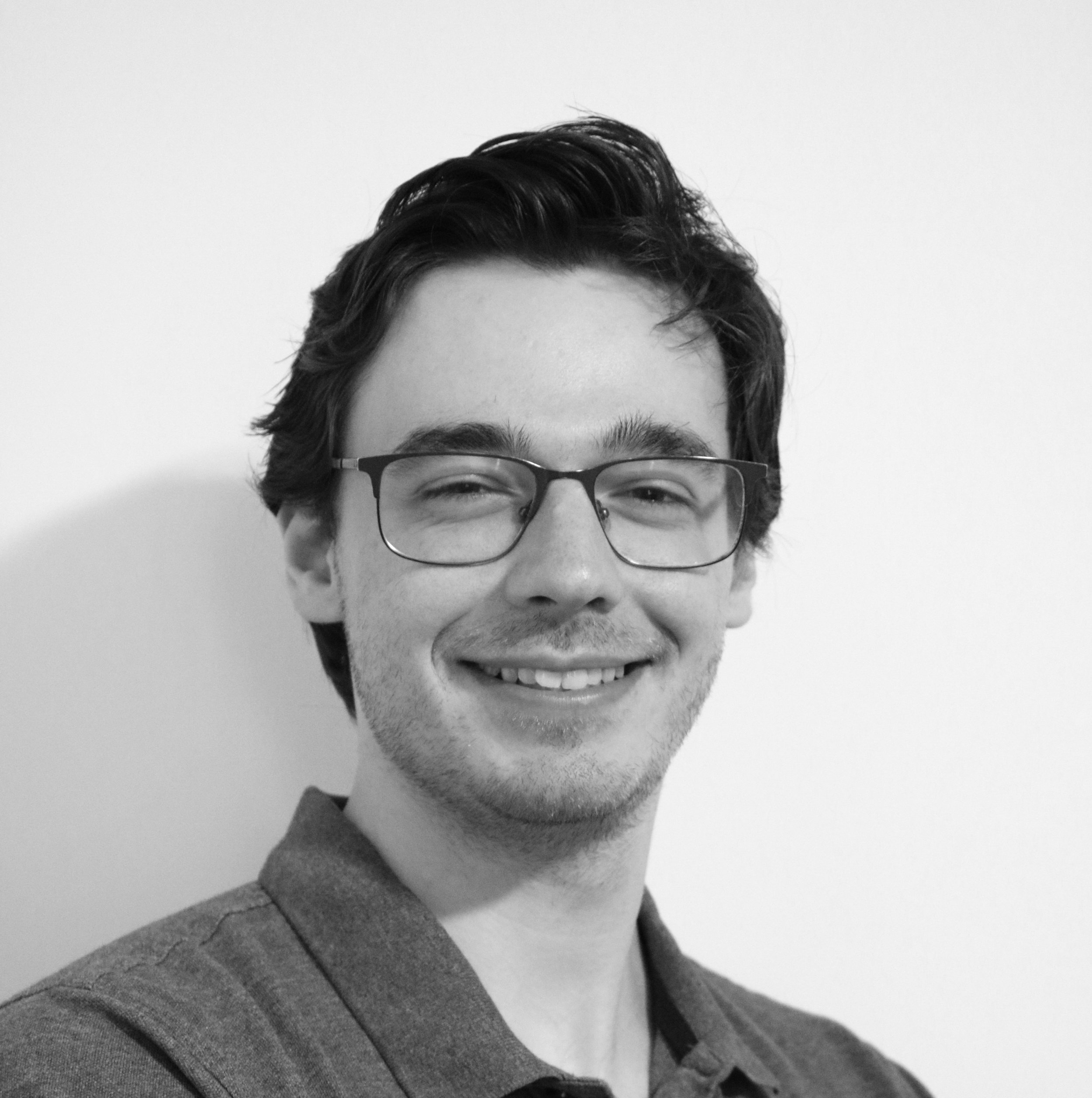 Black and white portrait of a young man with glasses, smiling, with dark, wavy hair, wearing a collared shirt, against a plain background.