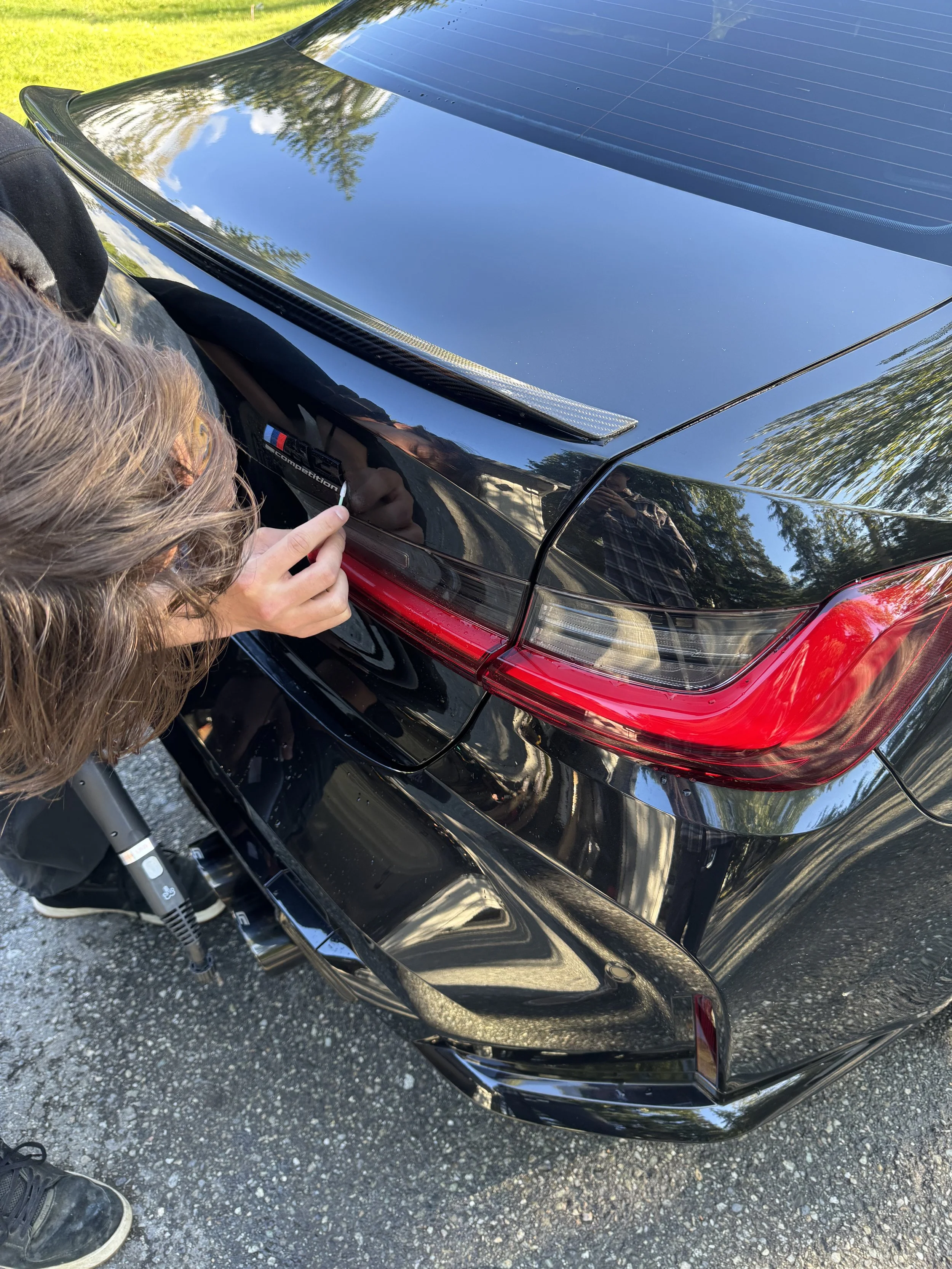 Person cleaning emblem sticker labeled 'm Performance' on the rear of a black sports car.