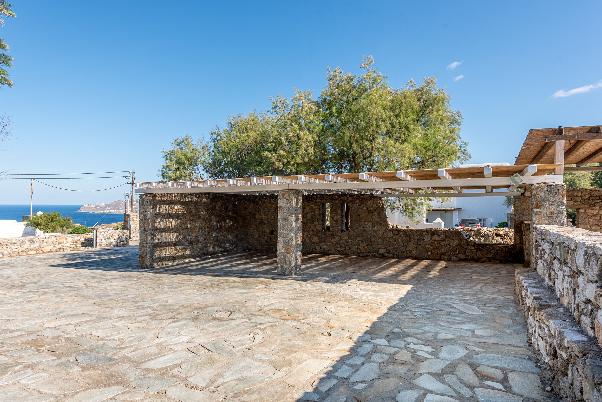 Large private parking area with stone paving, pergola-shading, and sea view at Villa Zanetti Mykonos.