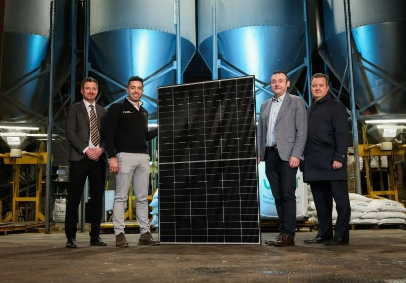 Four men standing beside a solar panel in front of feed silos at Capper Trading's Tamnamore site