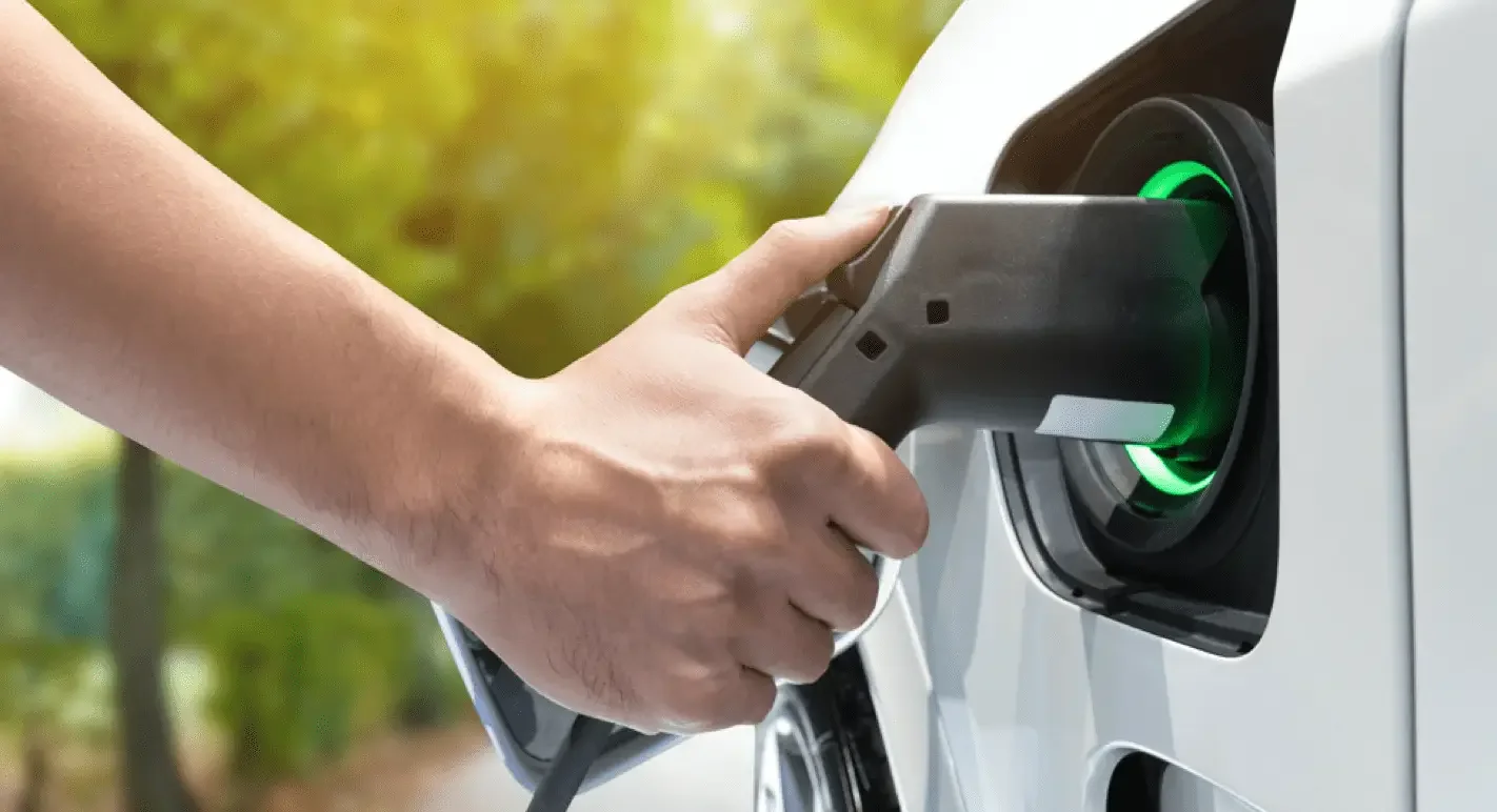 A person charging an electric vehicle at a charging station outdoors in a green environment.