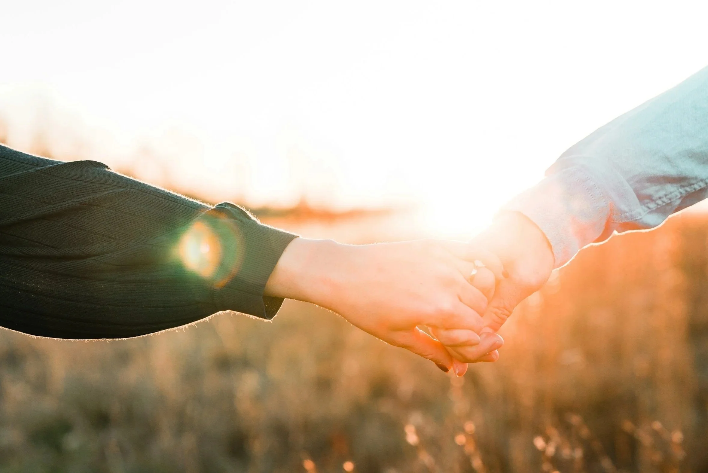 Two people holding hands outdoors during sunset with sunlight in the background.