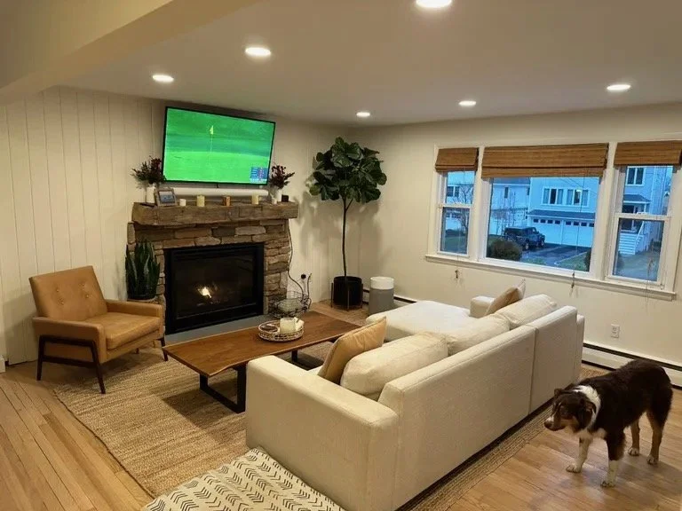 Living room with a white sofa, tan armchair, coffee table, fireplace, TV, and a dog near the sofa.