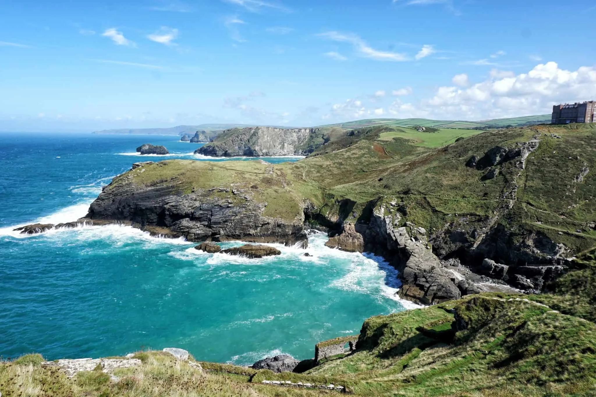 Coastal landscape with green cliffs, rocky shoreline, and blue ocean under a partly cloudy sky.