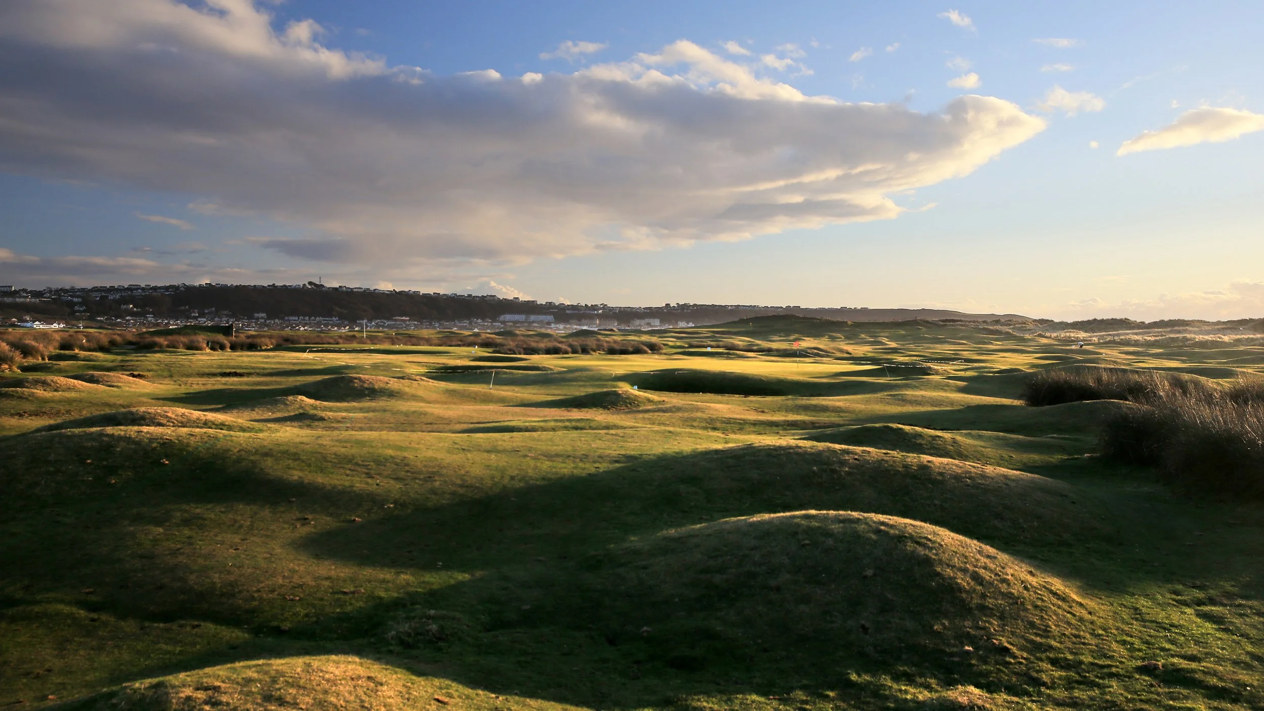 A golf course with green fairways and sand traps, under a partly cloudy sky during sunset or sunrise.