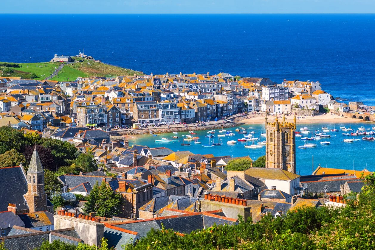 St Ives, a coastal town with colorful buildings, boats in the harbor, and a church tower overlooking the ocean.