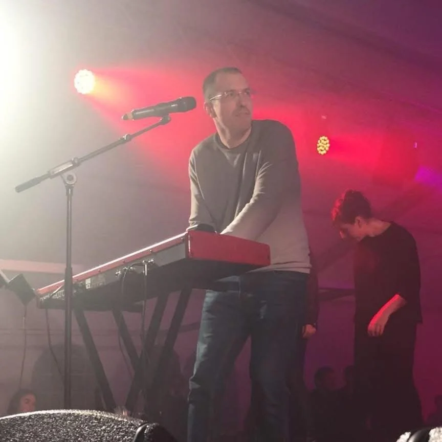 Gerard Pastor standing and playing a keyboard on a live stage, looking to the side while performing.