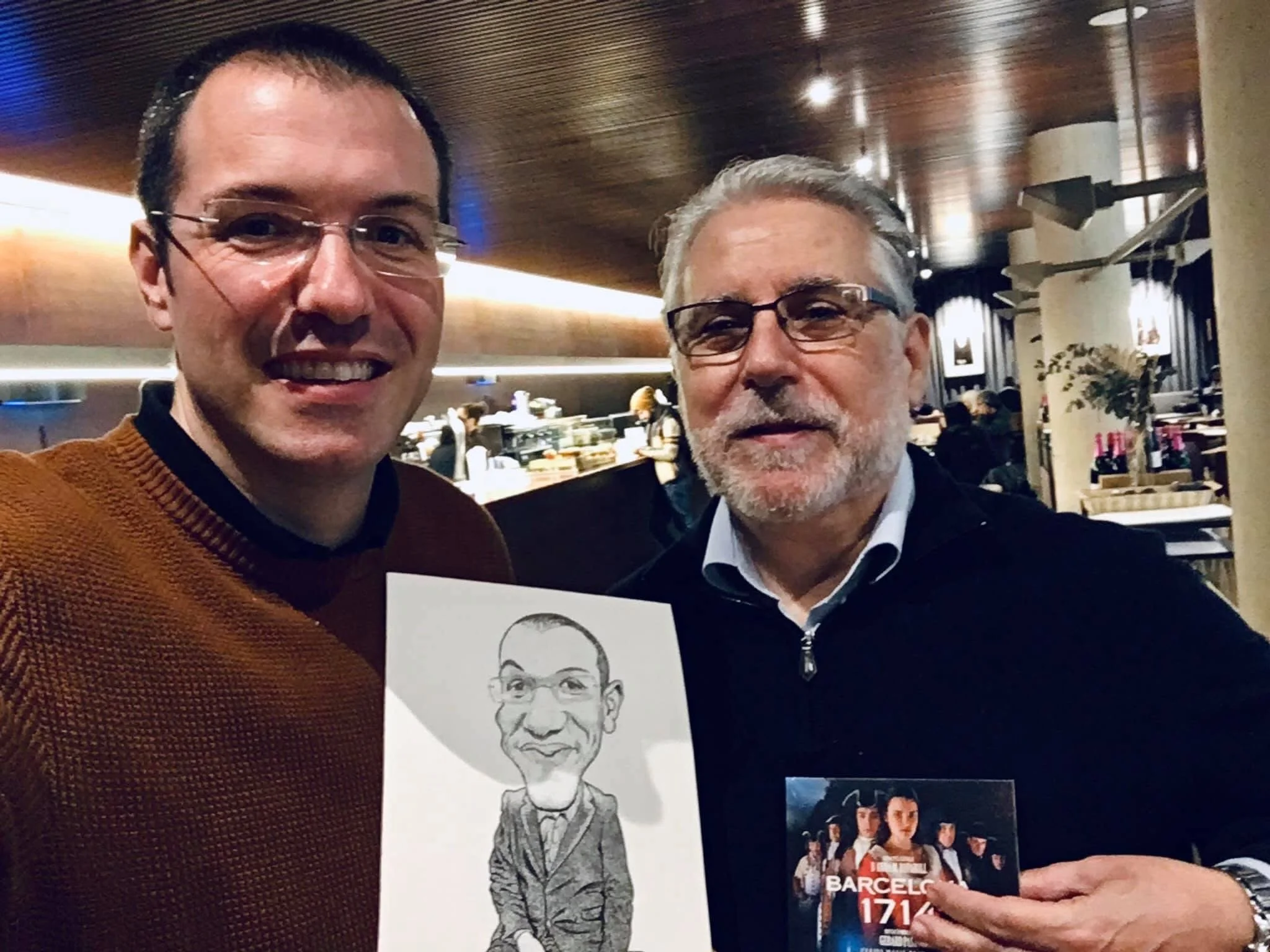 Photograph of Joan Bosch and Gerard Pastor smiling, with Gerard holding the caricature gifted to him by Joan Bosch.