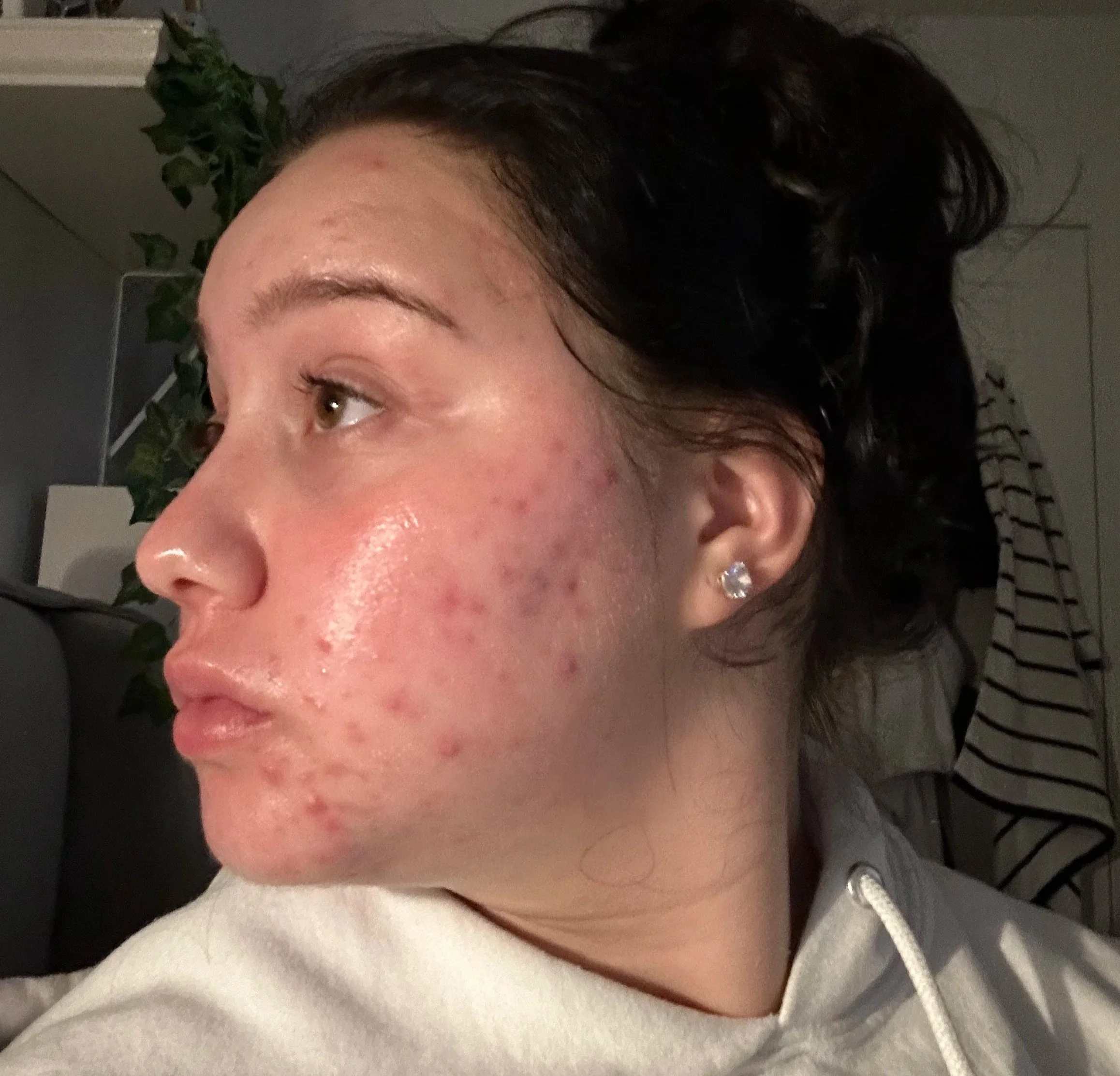 Close-up of a woman's face showing her eye, cheek, and part of her nose, with dark hair and wearing diamond stud earrings, in a dimly lit environment.