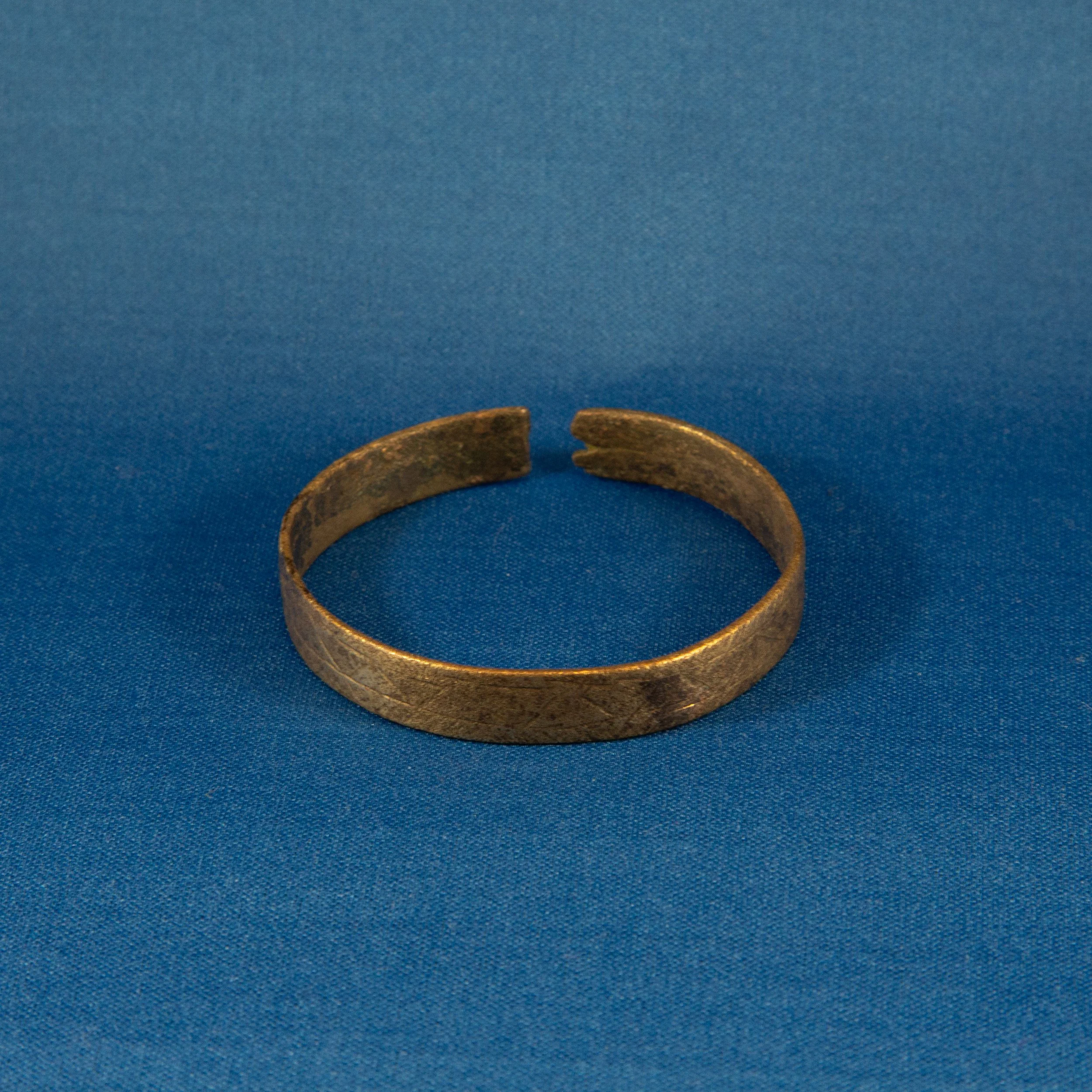 An open bronze or brass cuff bracelet with a textured surface, placed on a blue fabric background.