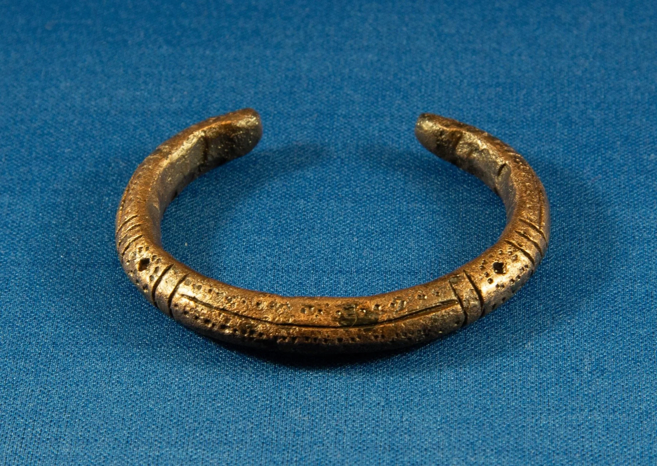 Ancient bronze bracelet with engraved patterns on a blue fabric background