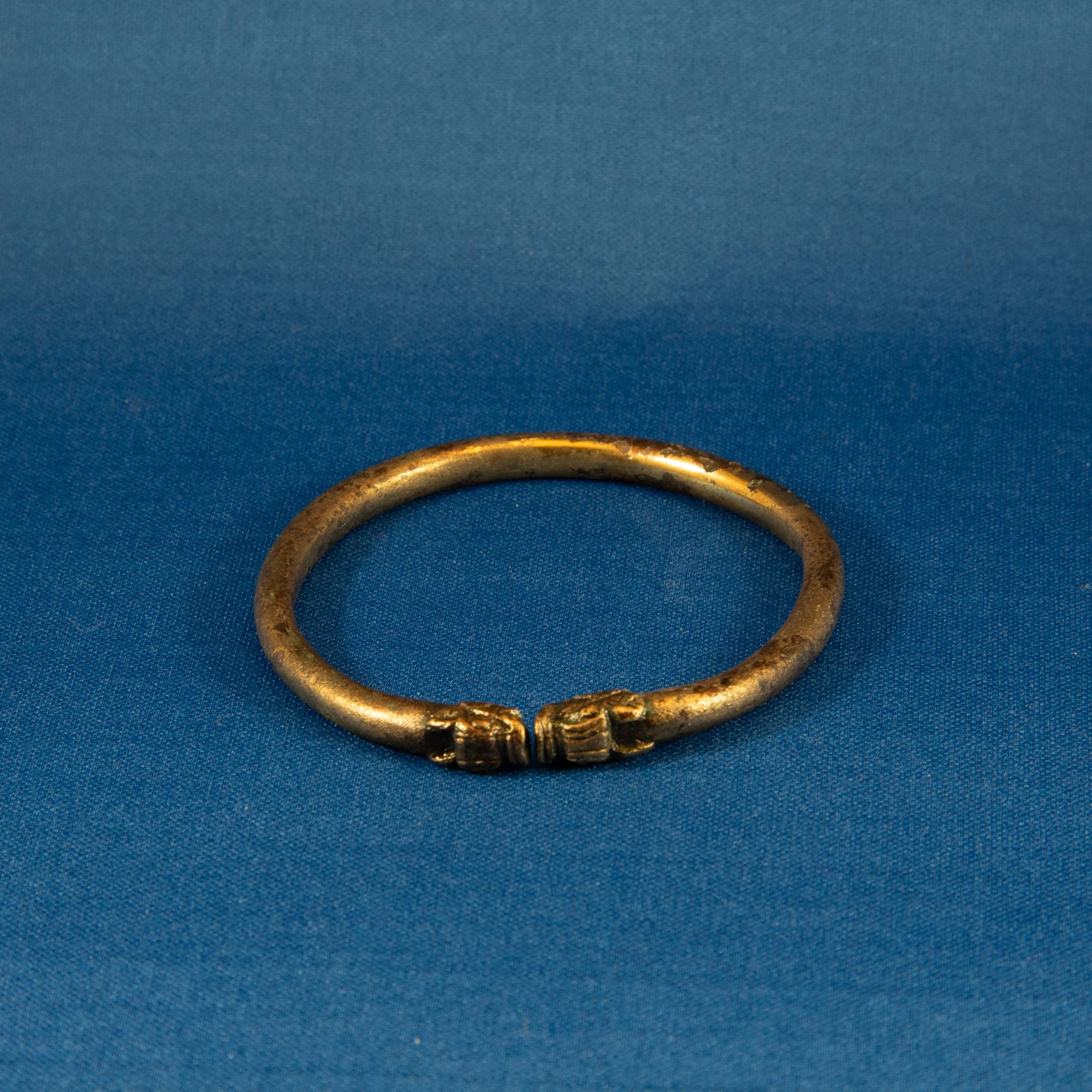 An ancient metallic bracelet with a simple band design, resting on a blue surface.