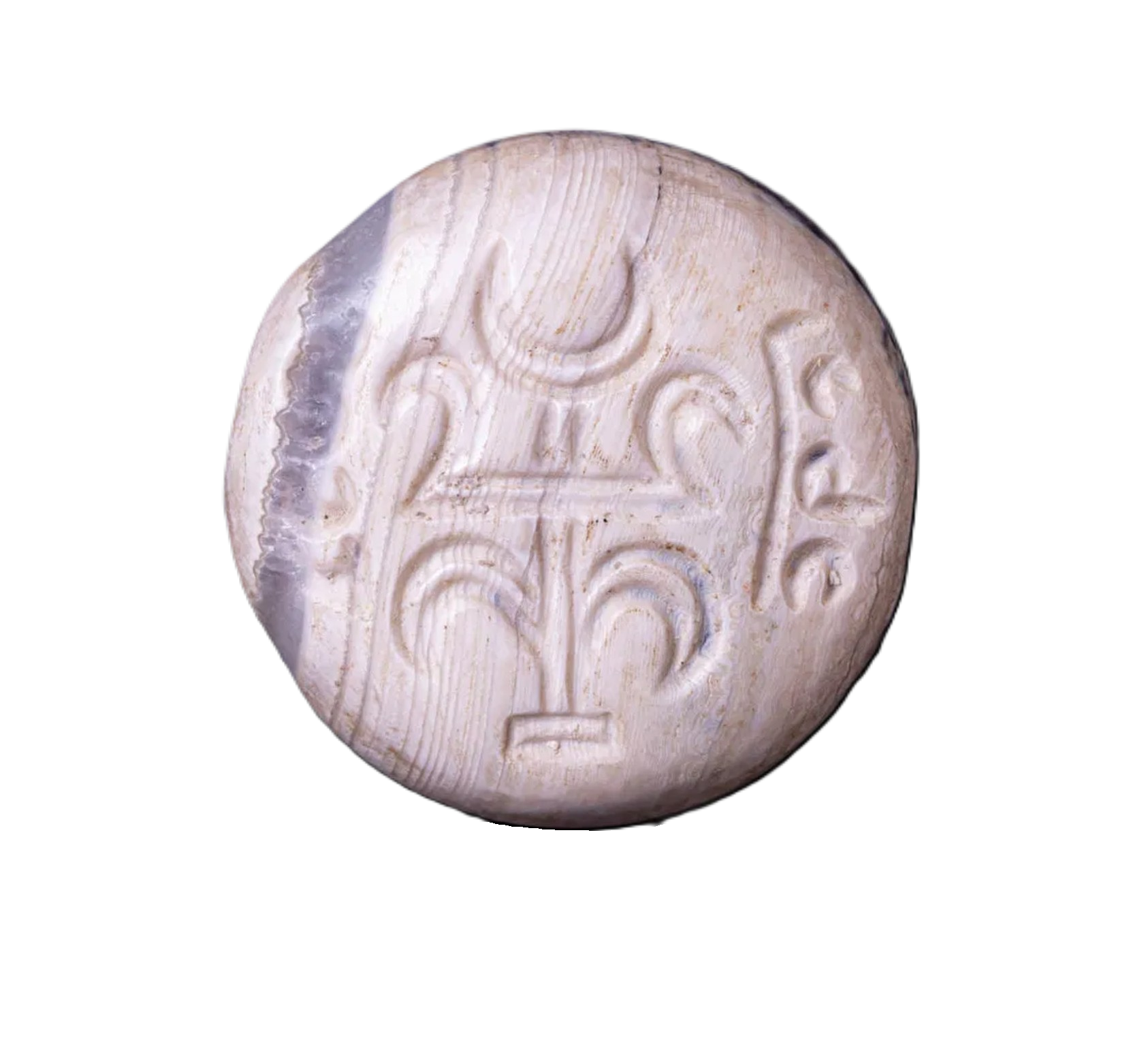 A carved ivory coin or token with ancient or tribal symbols, featuring a crescent moon and other geometric shapes, against a black background.