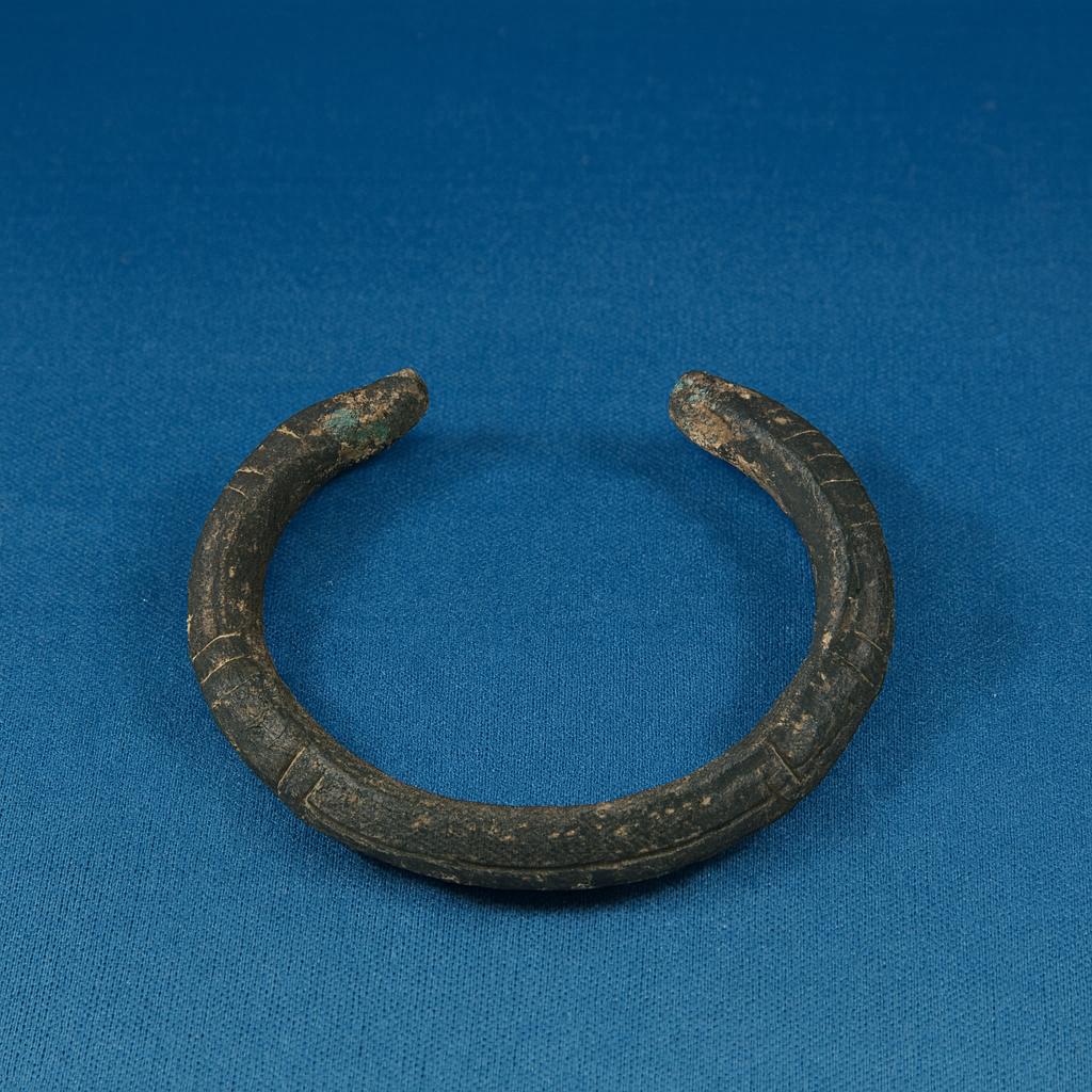 Ancient bronze bracelet with a weathered patina, lying on a blue background.