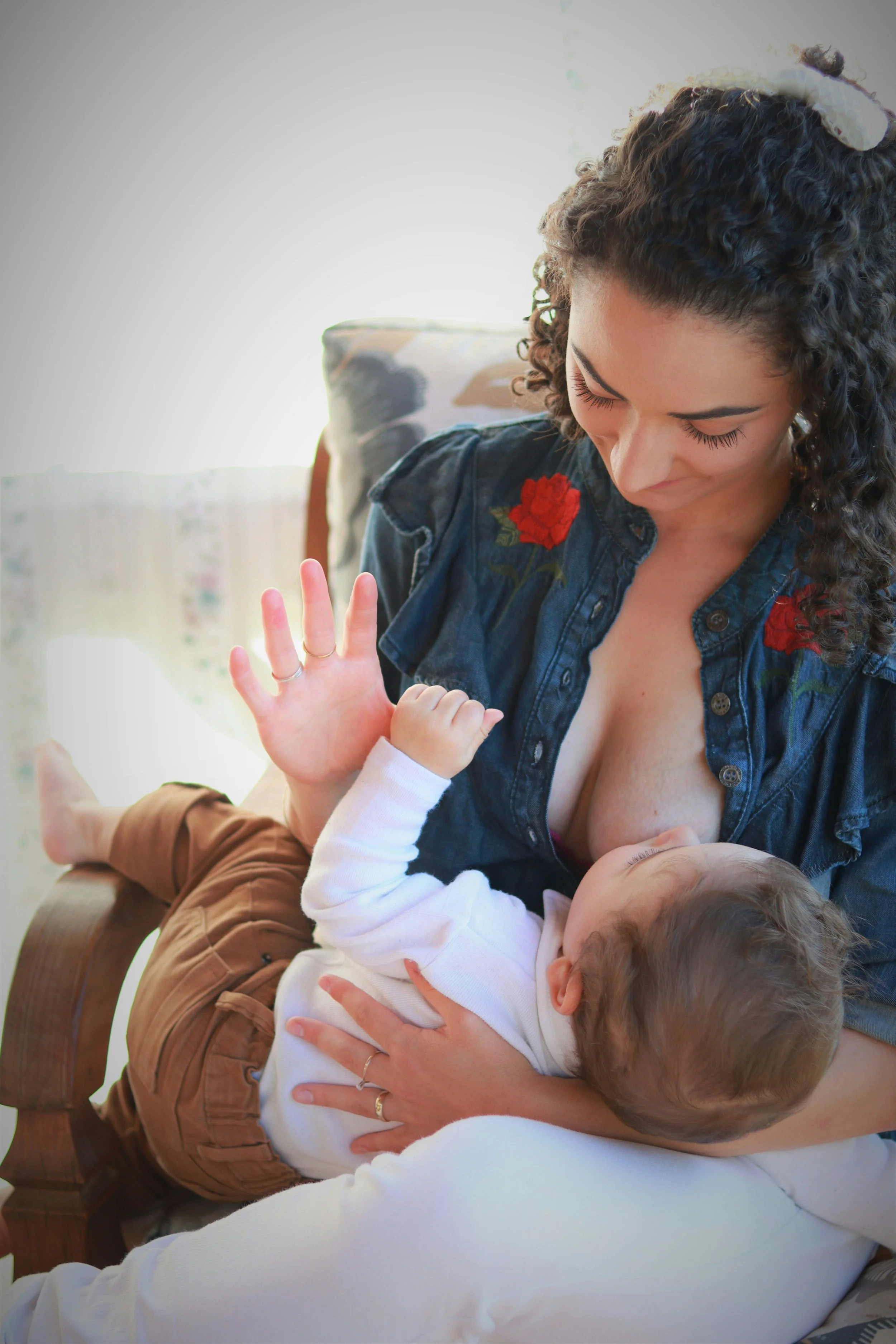 A woman breastfeeding a baby on her lap inside a room with natural light.