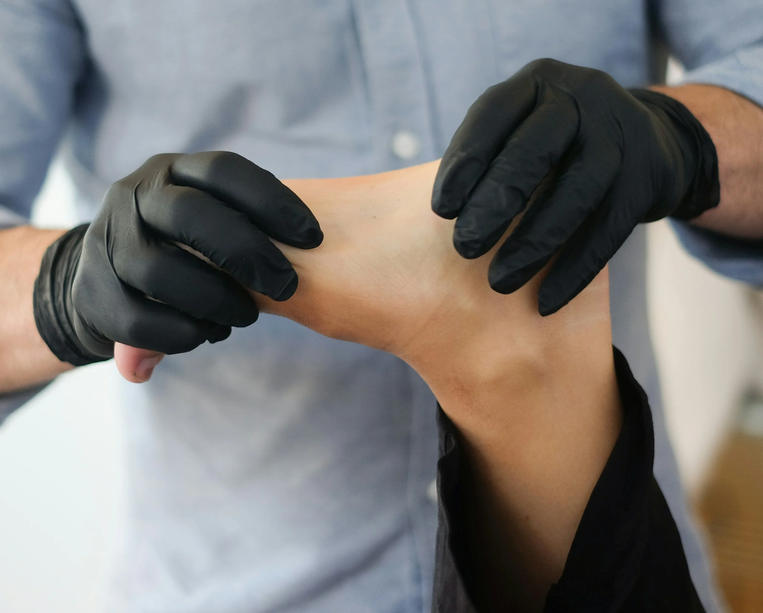 A person wearing black gloves is holding another person's arm during a medical or professional procedure.