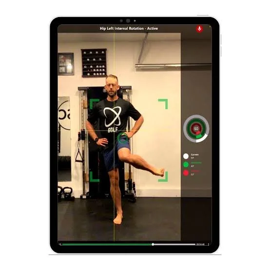 A man standing on one leg with his hands on his hips in a gym, captured by a tablet screen with a motion analysis app on display.