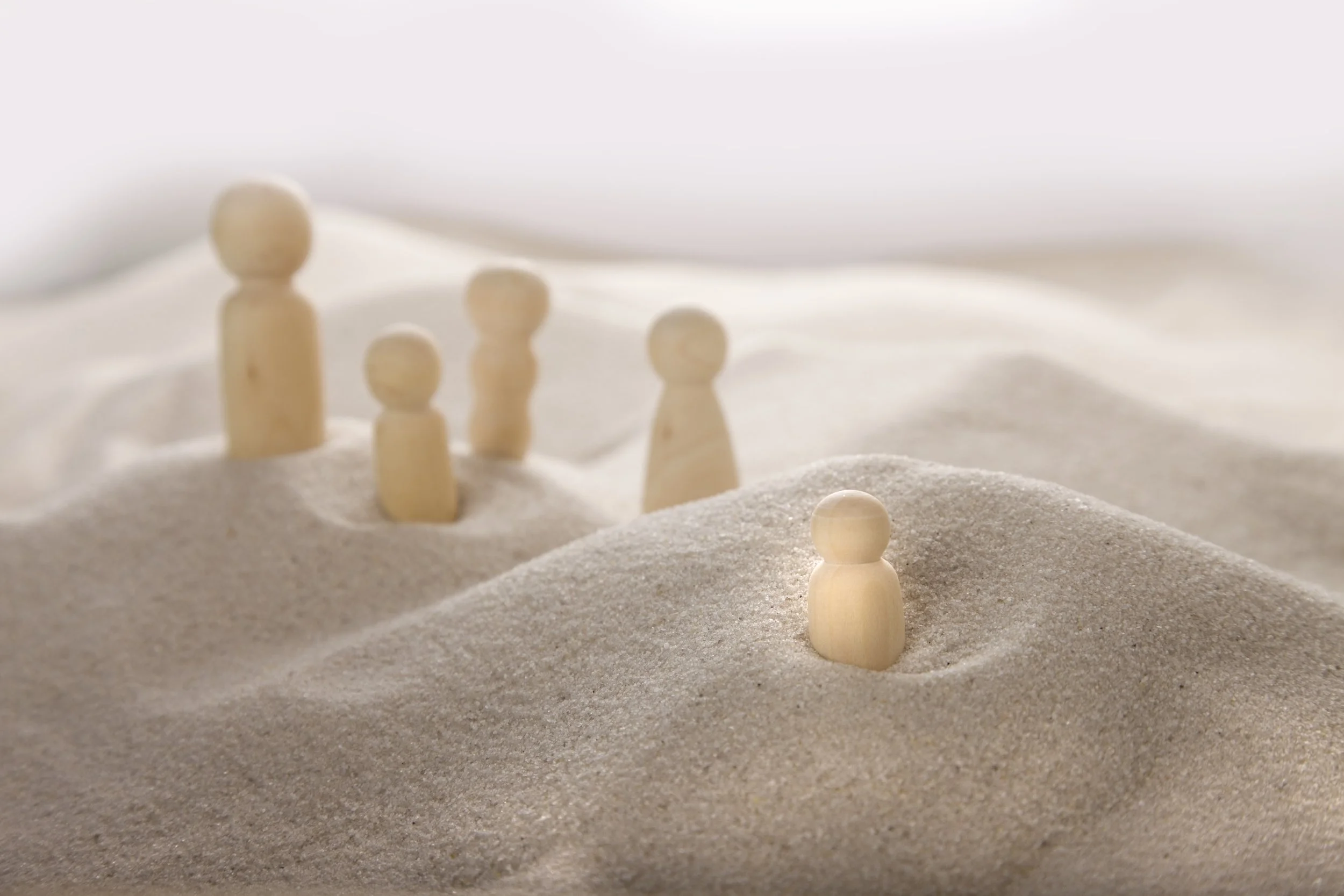 Small wooden figurines placed on white sandy terrain.