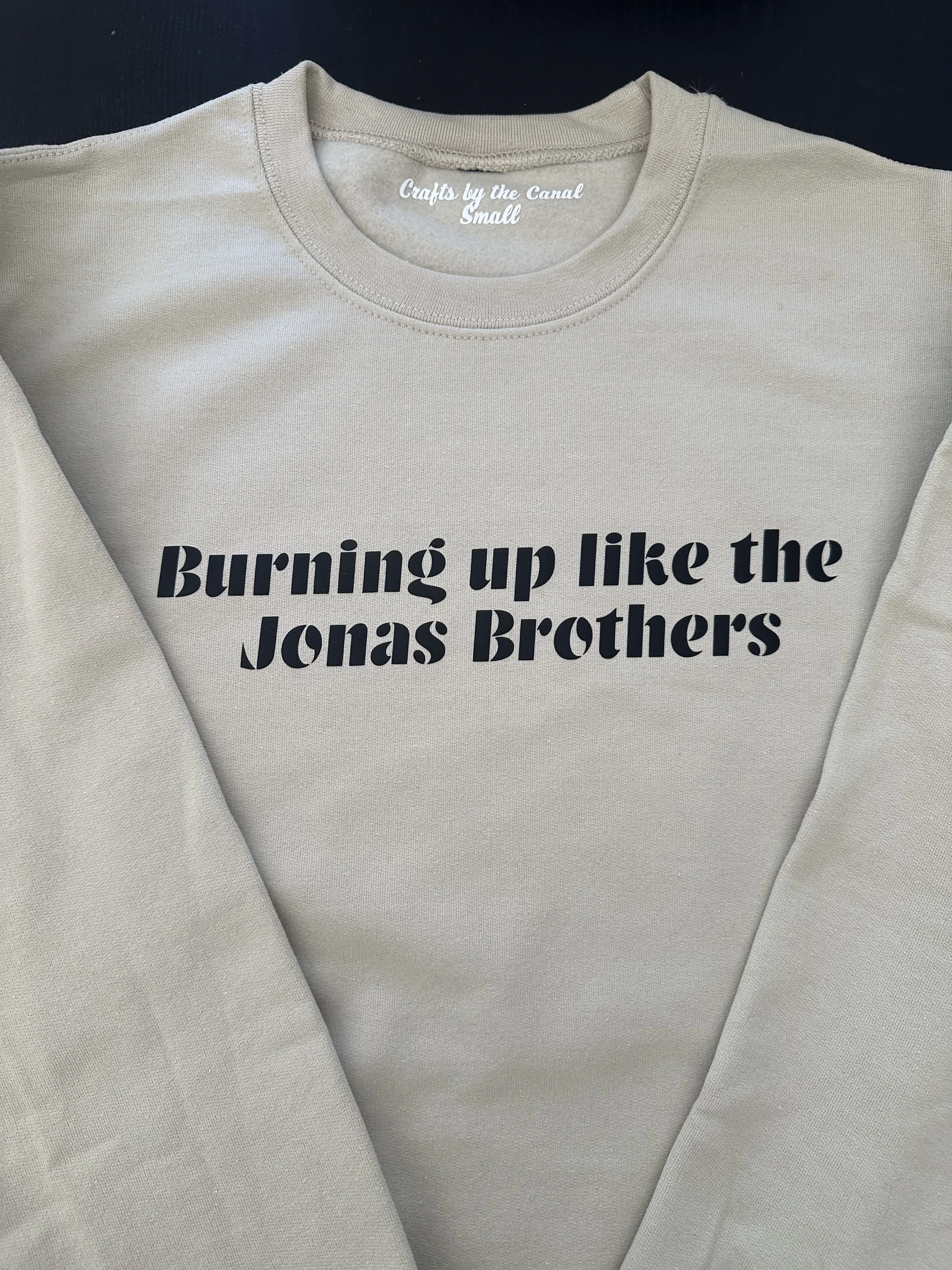 A beige sweatshirt with black text that reads, 'Burning up like the Jonas Brothers.'