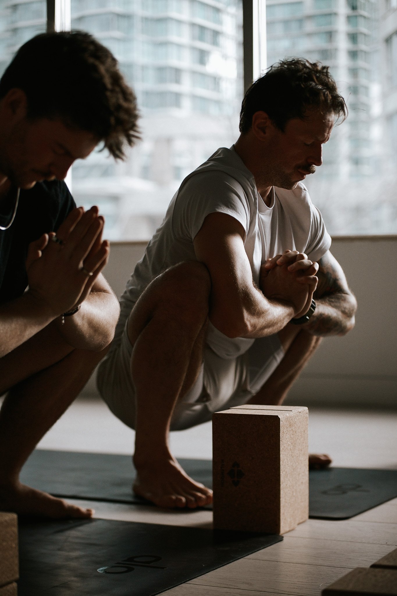 Group of people practicing yoga or meditation in a bright room, kneeling with their hands in prayer position, eyes closed, and focused expressions.