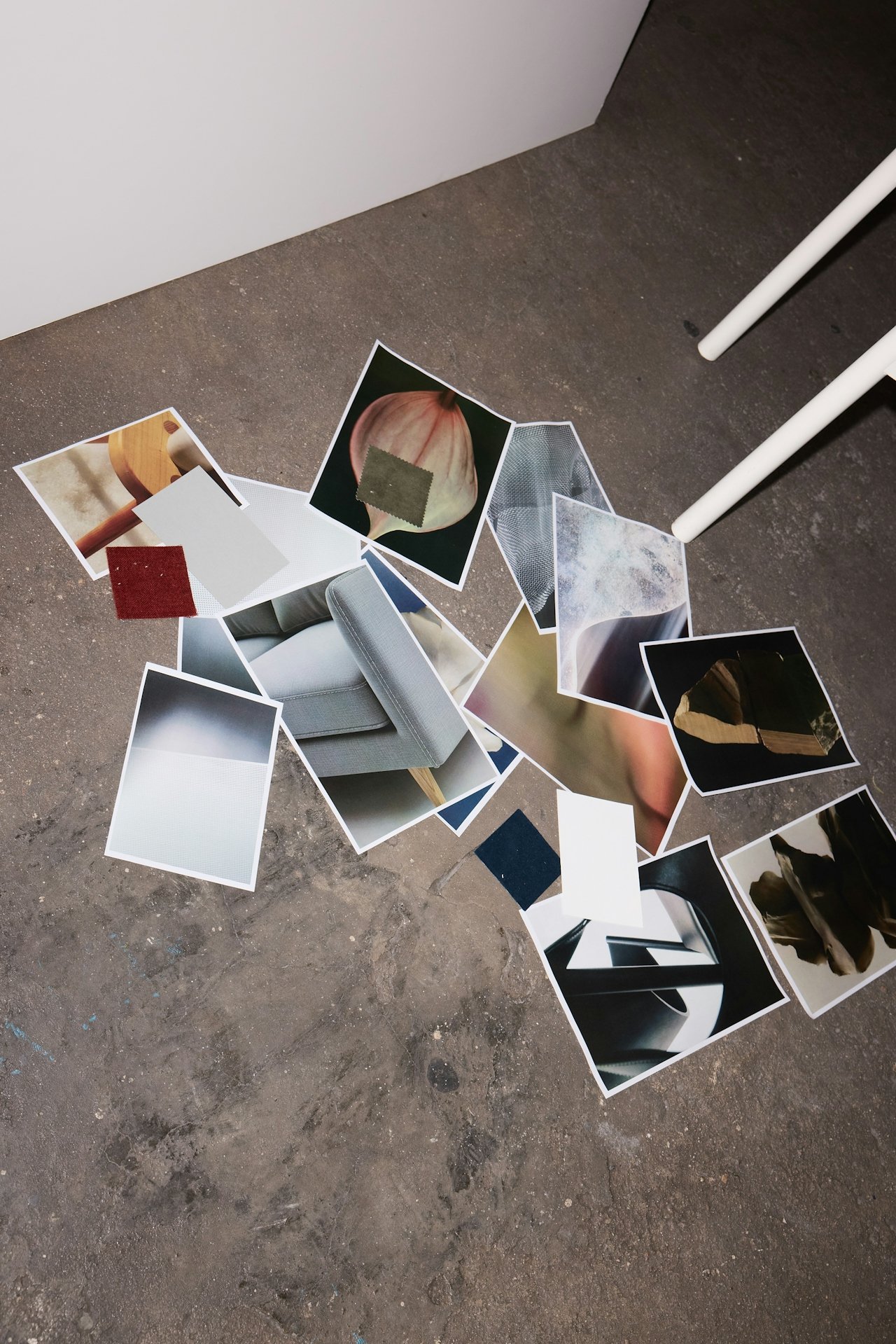 Scattered printed photos of various objects and scenes on a concrete floor, with two white legs of a piece of furniture visible in the background.
