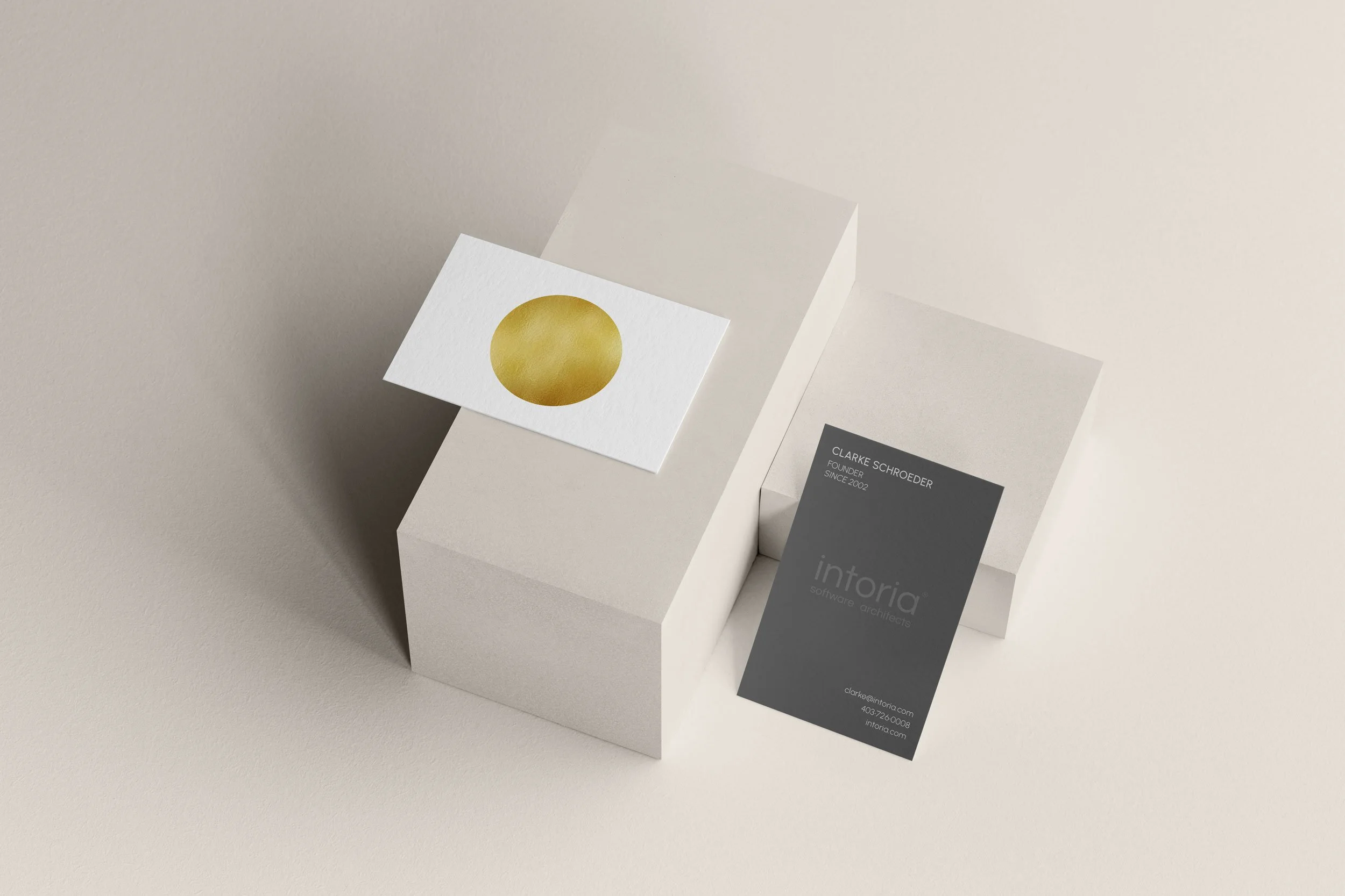 Business card with a large gold circle on a white background and another card with black and gray sections, placed on a white geometric block on a beige surface.