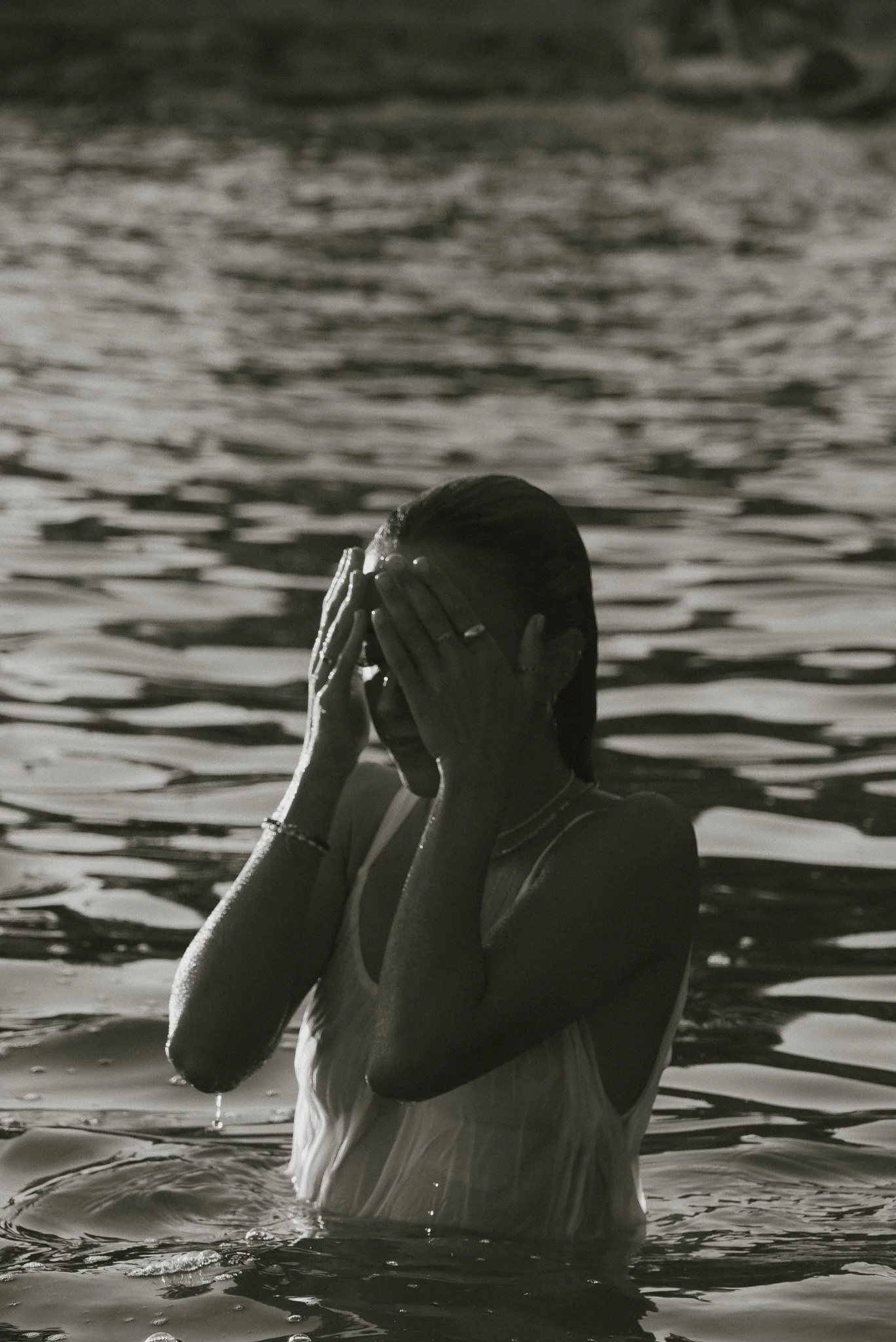 A person standing in water, covering their face with hands, during a rainy and overcast day.